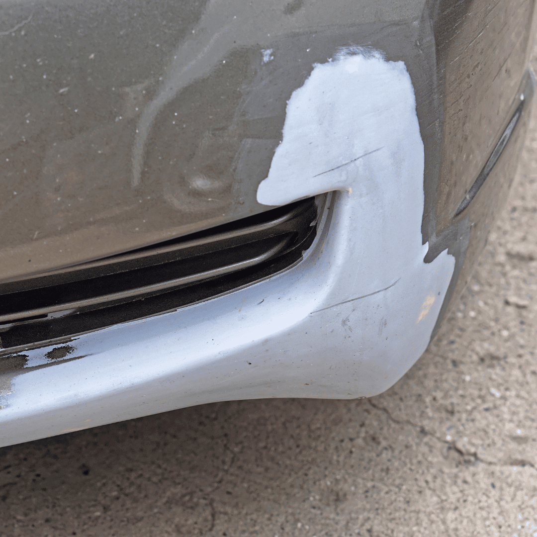 Close-up of a silver car's front bumper with a scratch and paint damage near the grille.