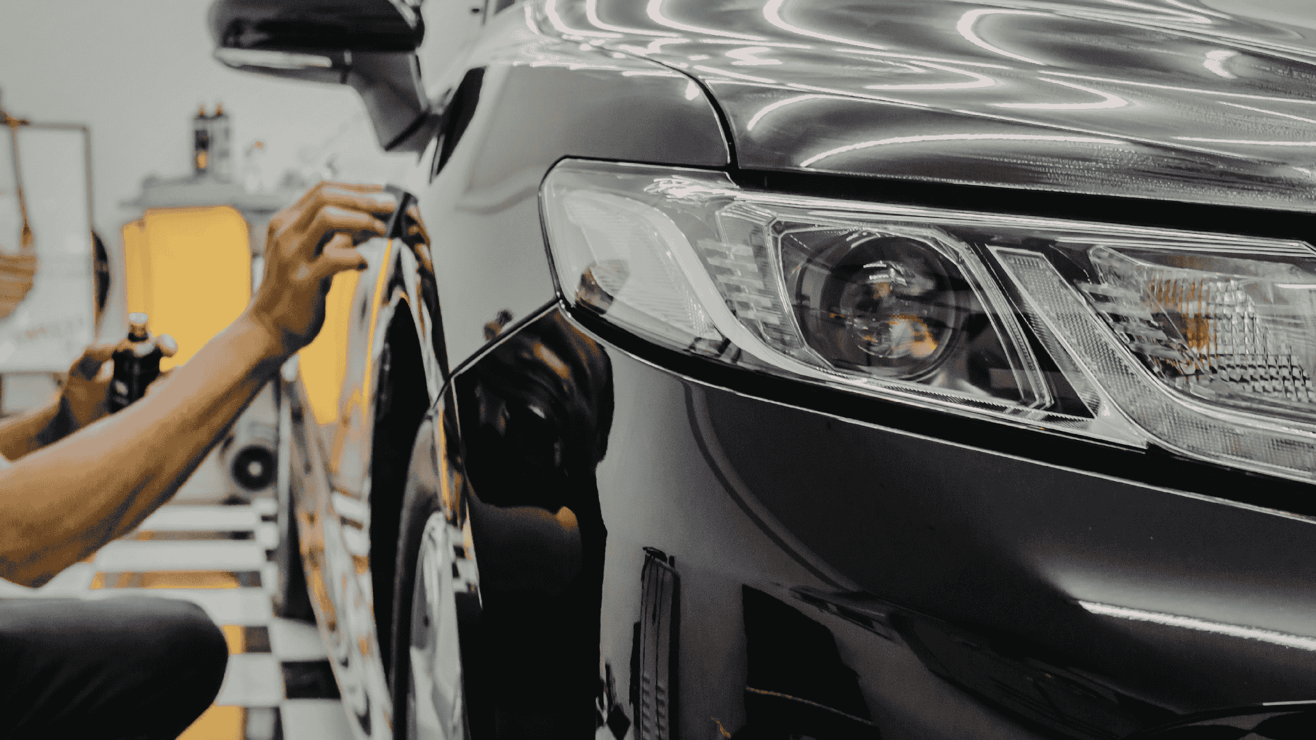 Close-up of a person’s hand working on a black car in a garage or workshop.