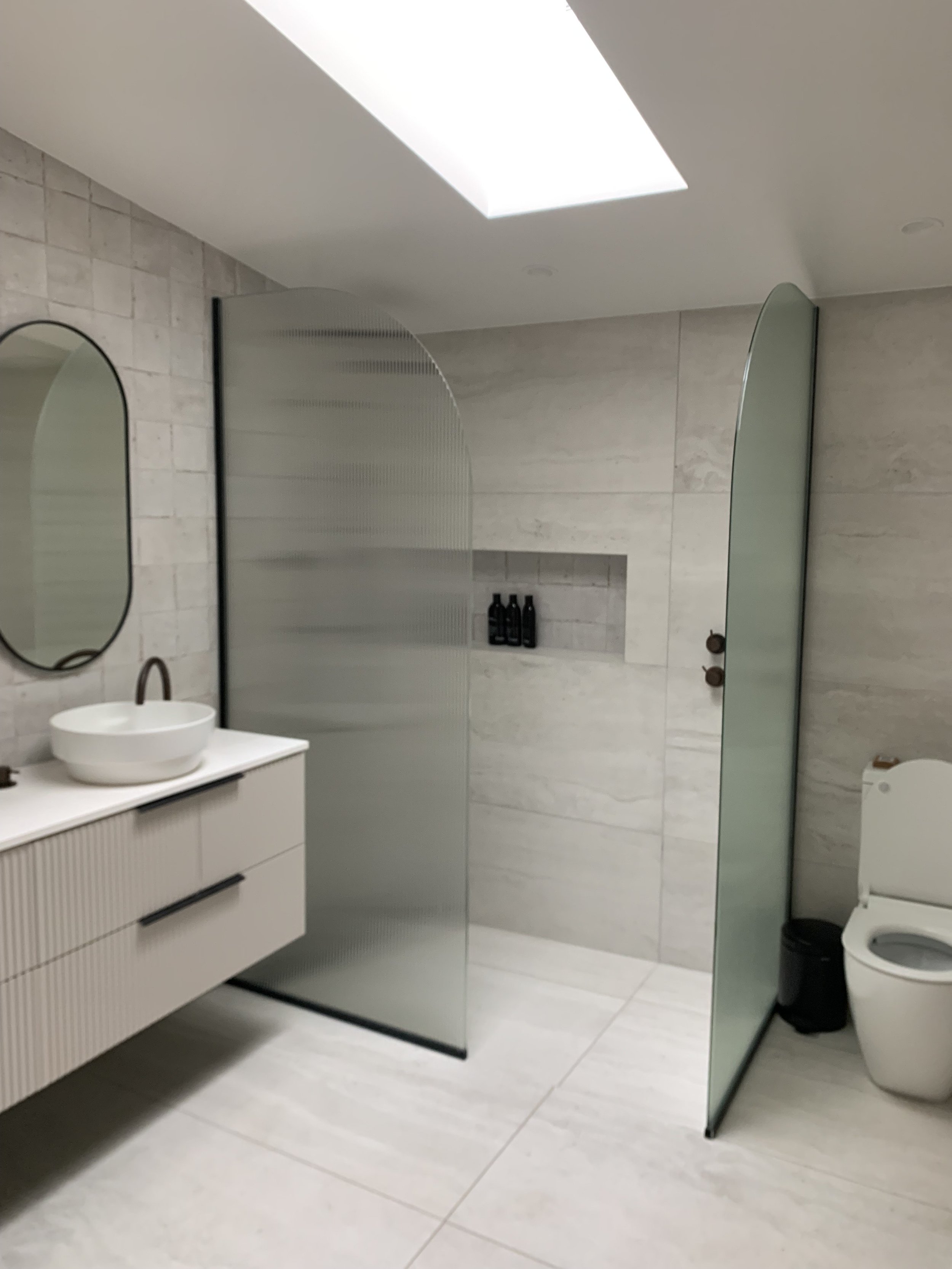 Modern bathroom with a walk-in shower, a white vanity with a round vessel sink, a mirror, and neatly rolled towels underneath the sink.