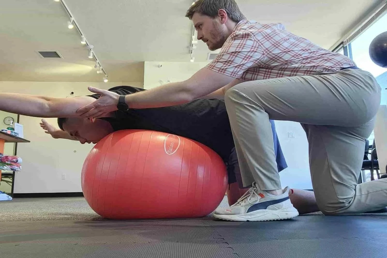 A physical therapist assists a patient with a neck and shoulder stability exercise to strengthen their postural muscles and reduce recurring neck pain and headaches
