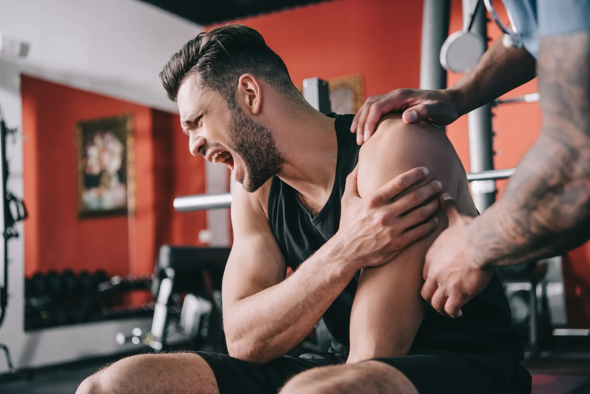 A man in a gym grabs his shoulder in pain after a bad lift. He would be an excellent candidate for our shoulder rehab program.