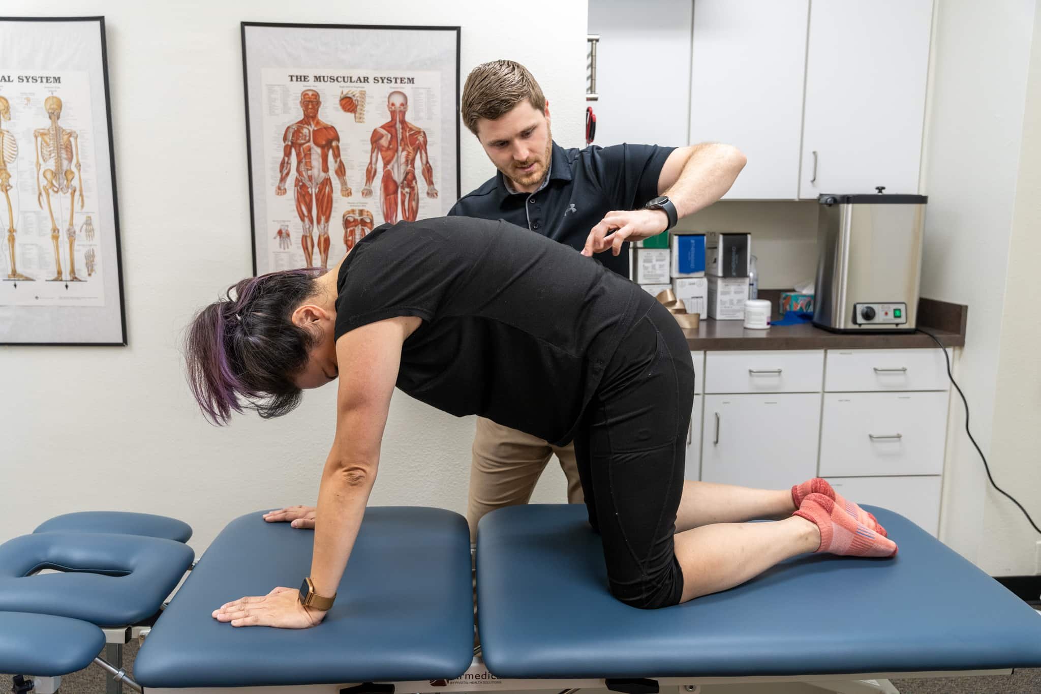 A physical therapist in a PT exam room working with a patient who has sciatica pain on their spinal mobility