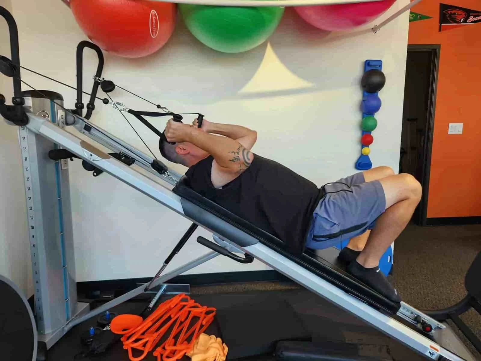 Man exercising on an inclined fitness machine, pulling resistance cables for a deloaded pull up as part of their workers' compensation rehab