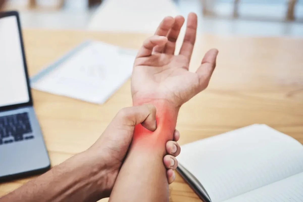 A person holds their wrist in pain from repetitive typing on their laptop.