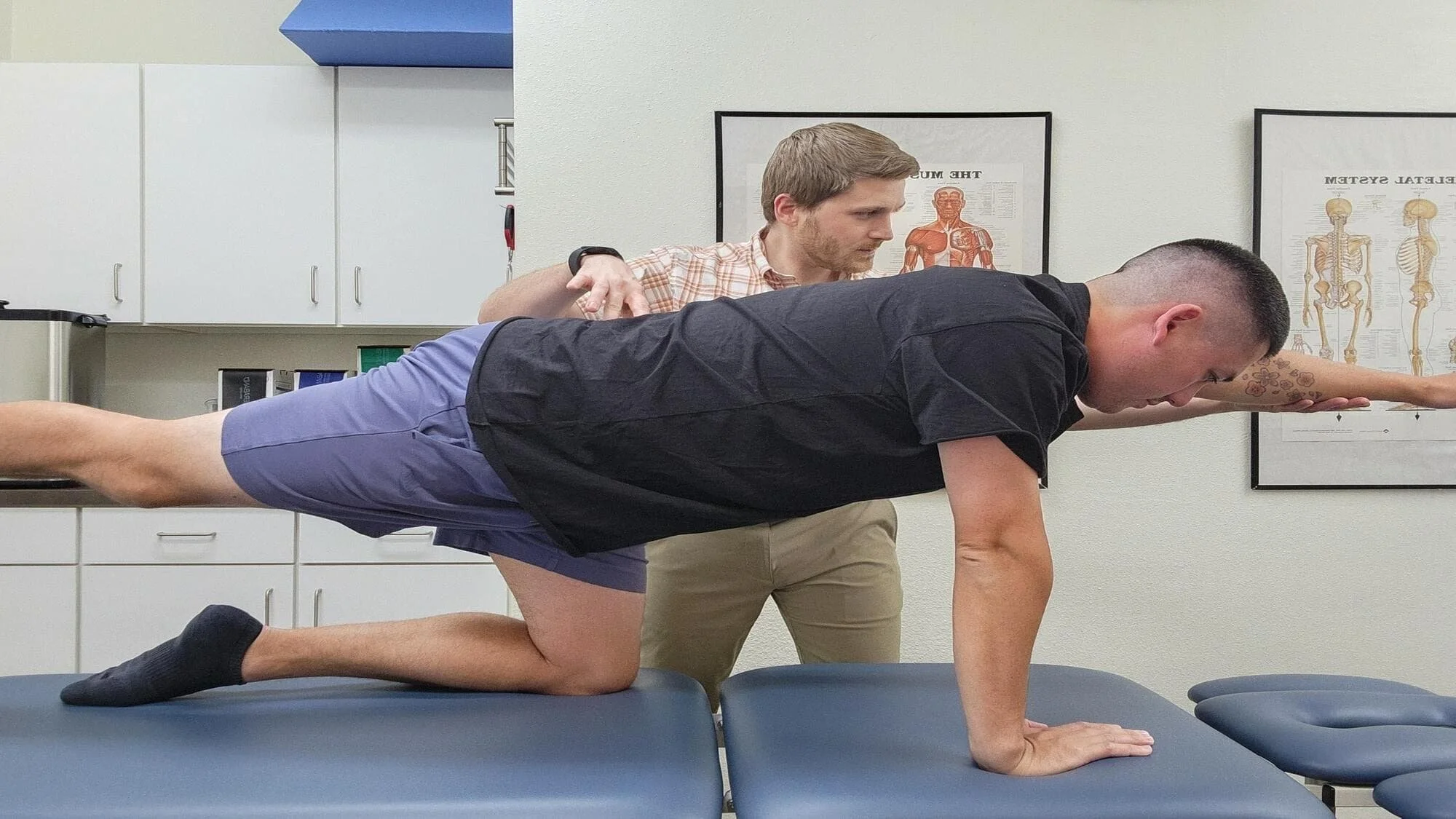A man performing a bird dog exercise while guided by a physical therapist for core and gluteal engagement.
