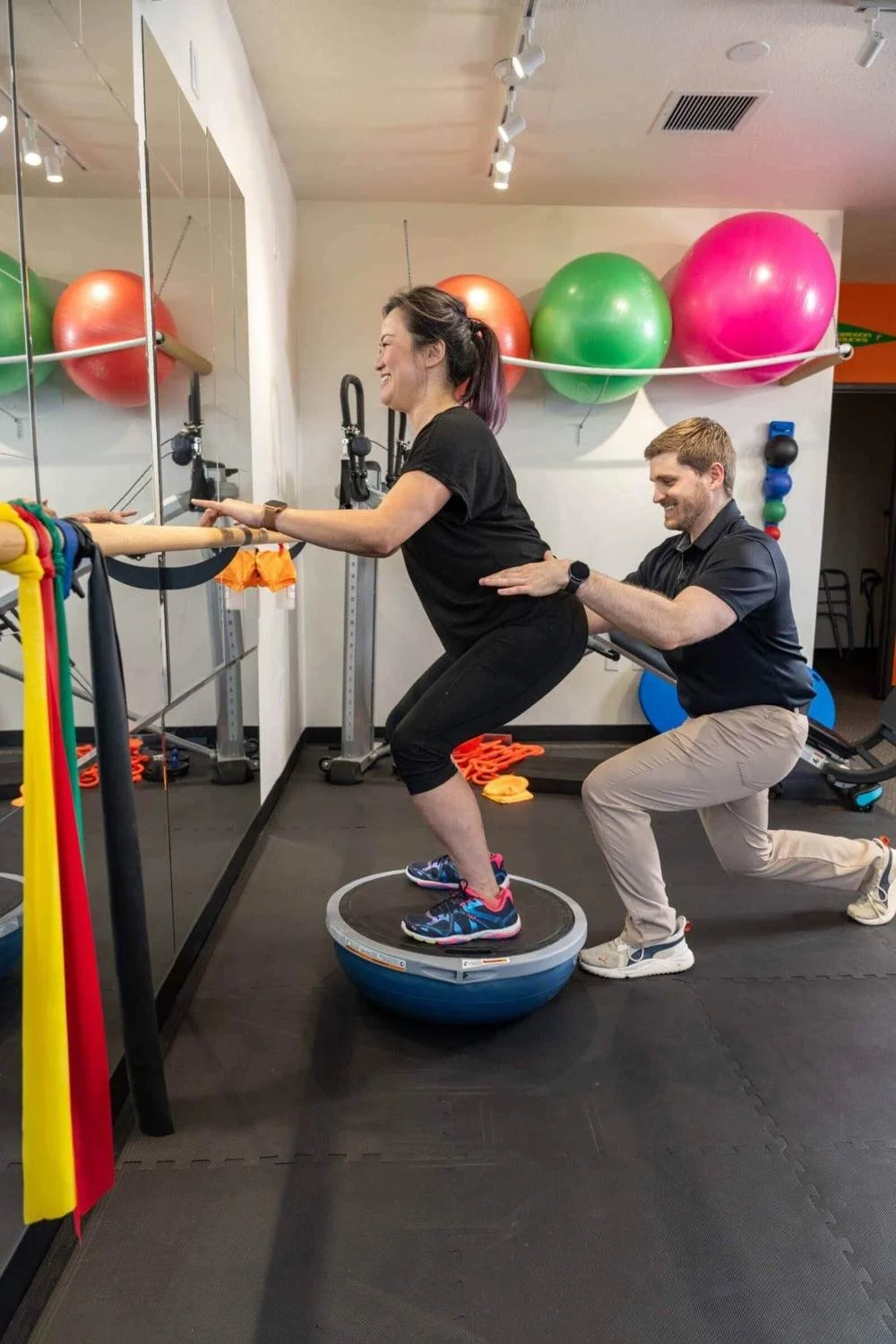 A physical therapist guards a patient as they perform BOSU squats for hamstring tendon pain rehab in Hillsboro, OR