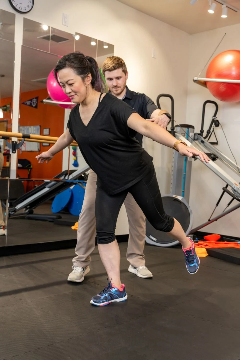A physical therapist guarding a patient as they perform a single-leg hip hinge while receiving treatment for side hip pain in Hillsboro, OR