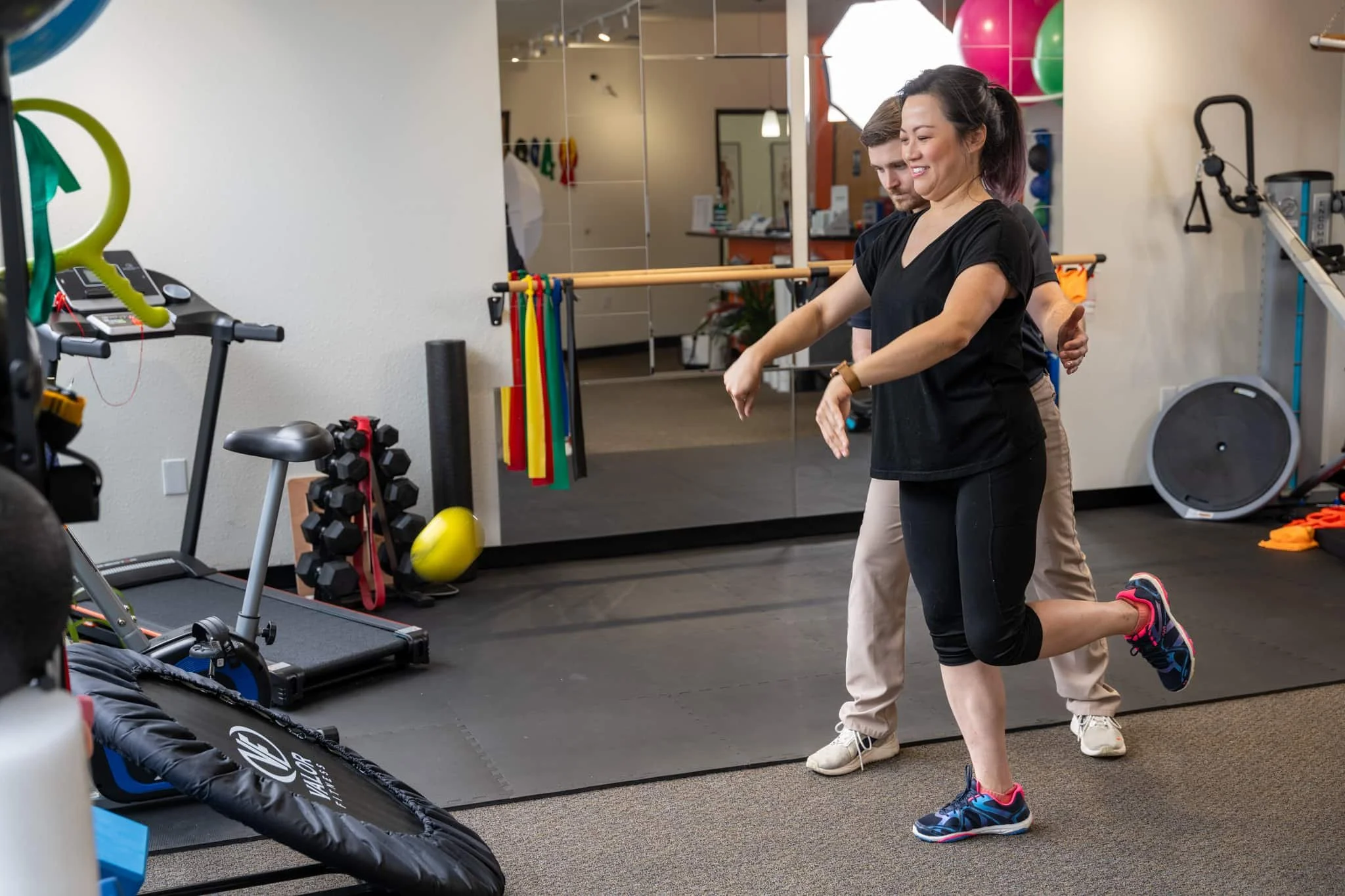 A patient performing a single-leg stance while tossing a weighted ball at a rebounder to work on balance and fall-prevention physical therapy