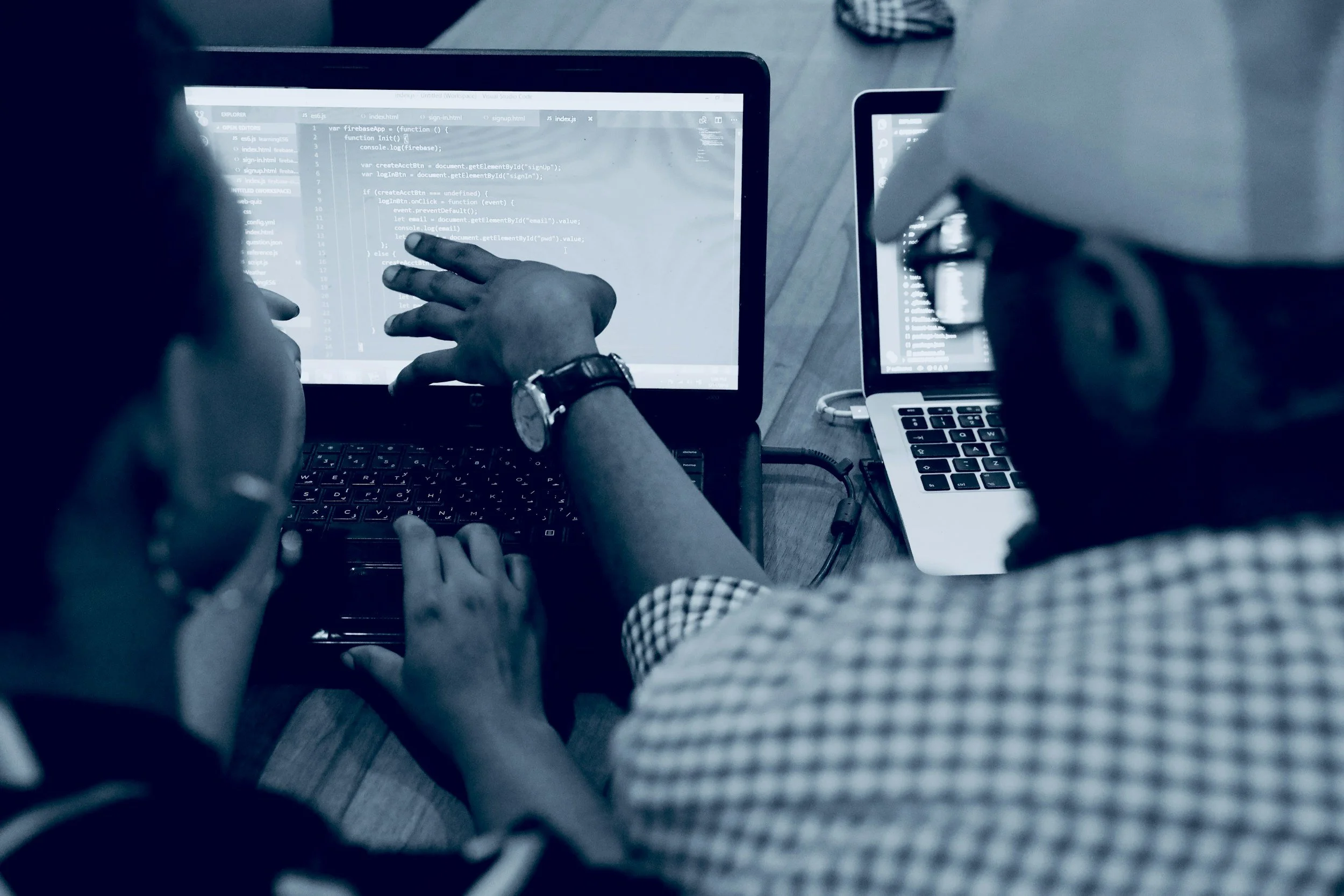 Two people collaborating on a project with a laptop displaying code, in a workspace setting.