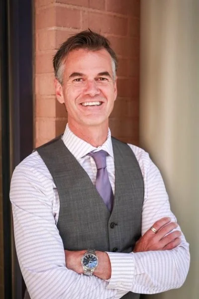 professional headshot of man wearing button down shirt, purple tie, and grey vest