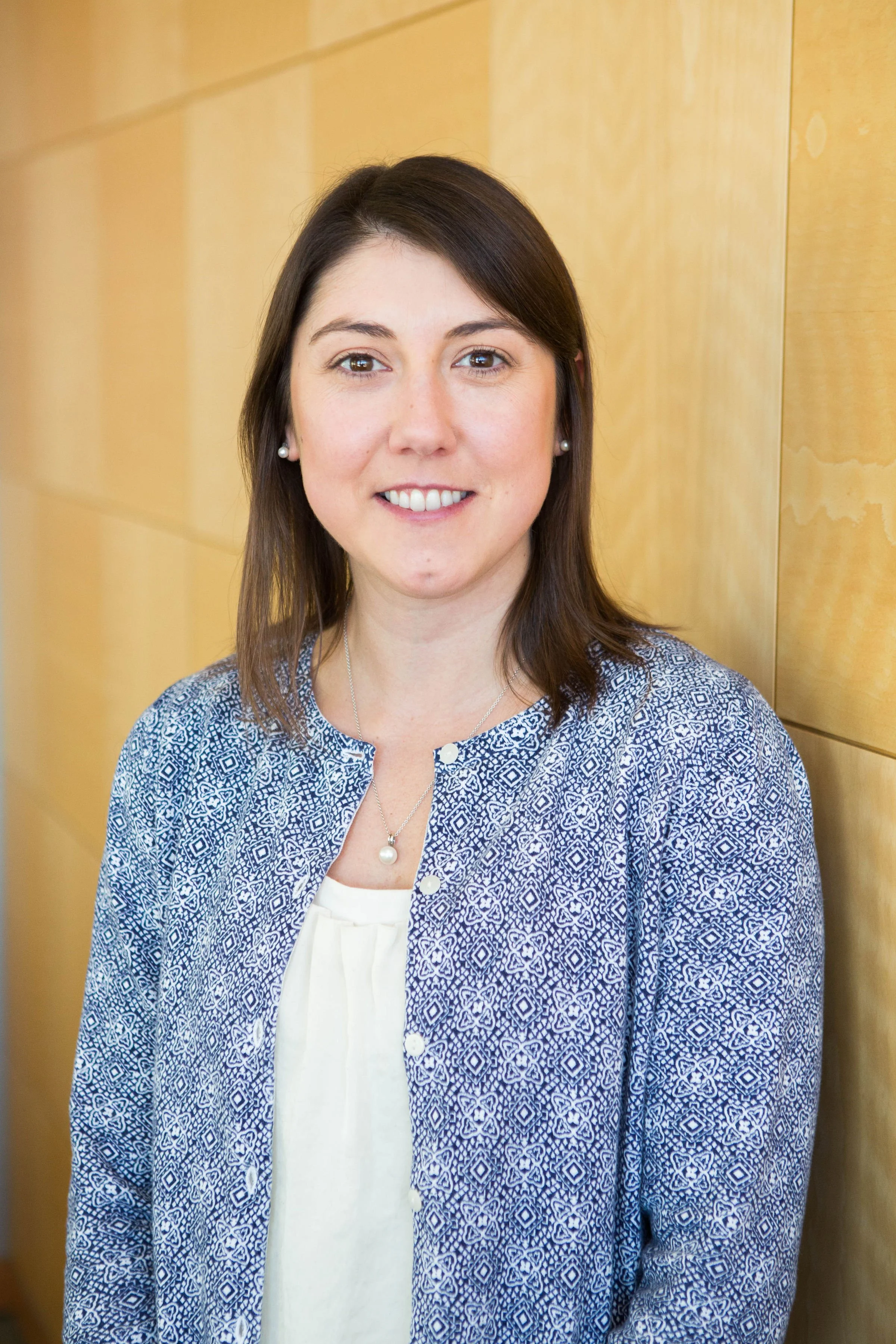 Professional headshot of brunette woman wearing white shirt under a blue and white cardigan