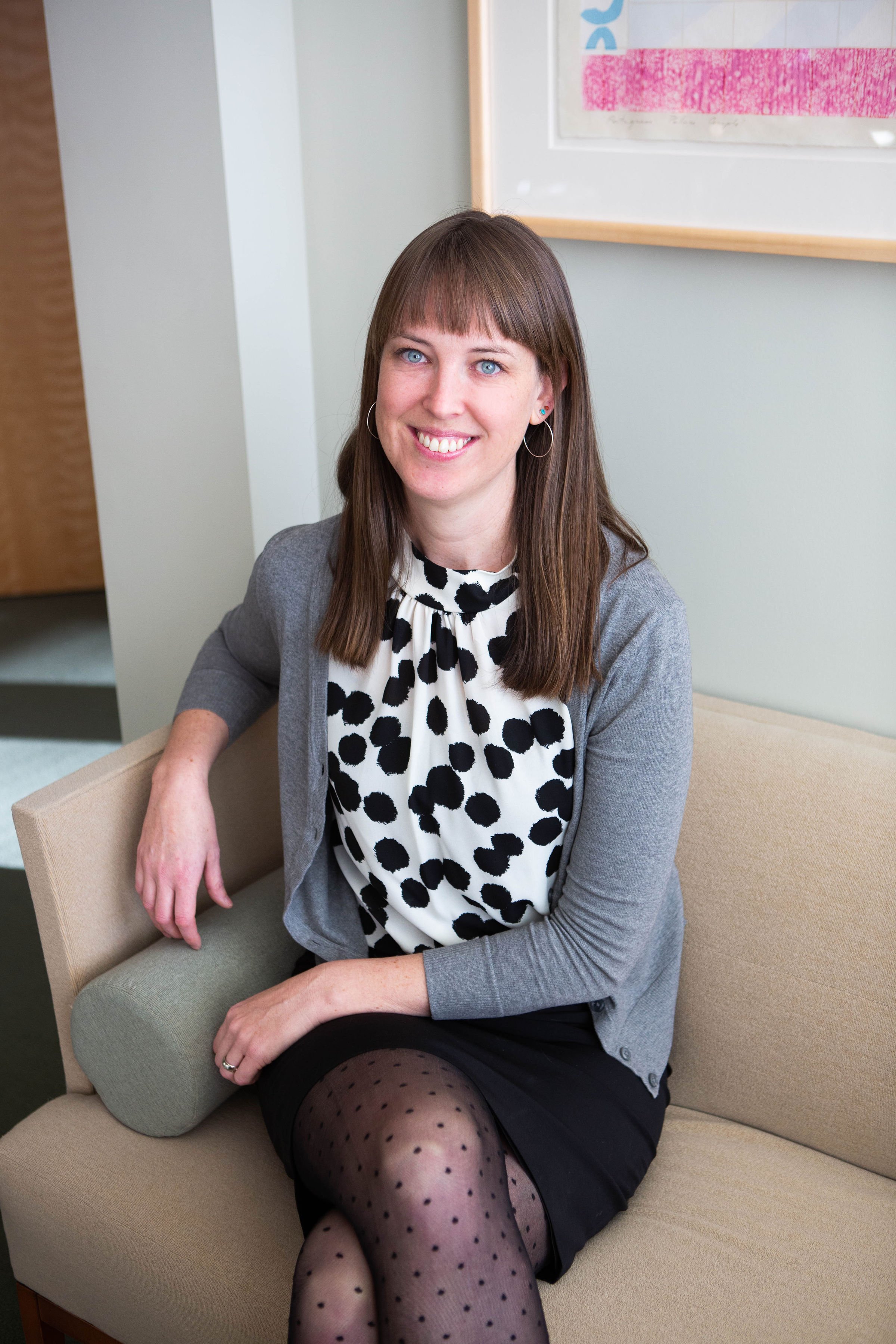 Woman sitting on couch, wearing grey cardigan over black and white polka dot top