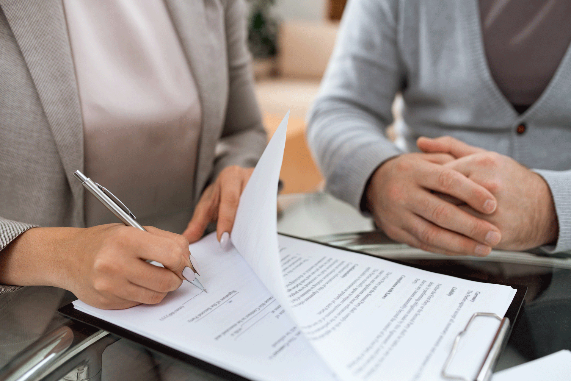 A close-up of two people at a table, one signing a document with a pen, implying a contract or agreement.