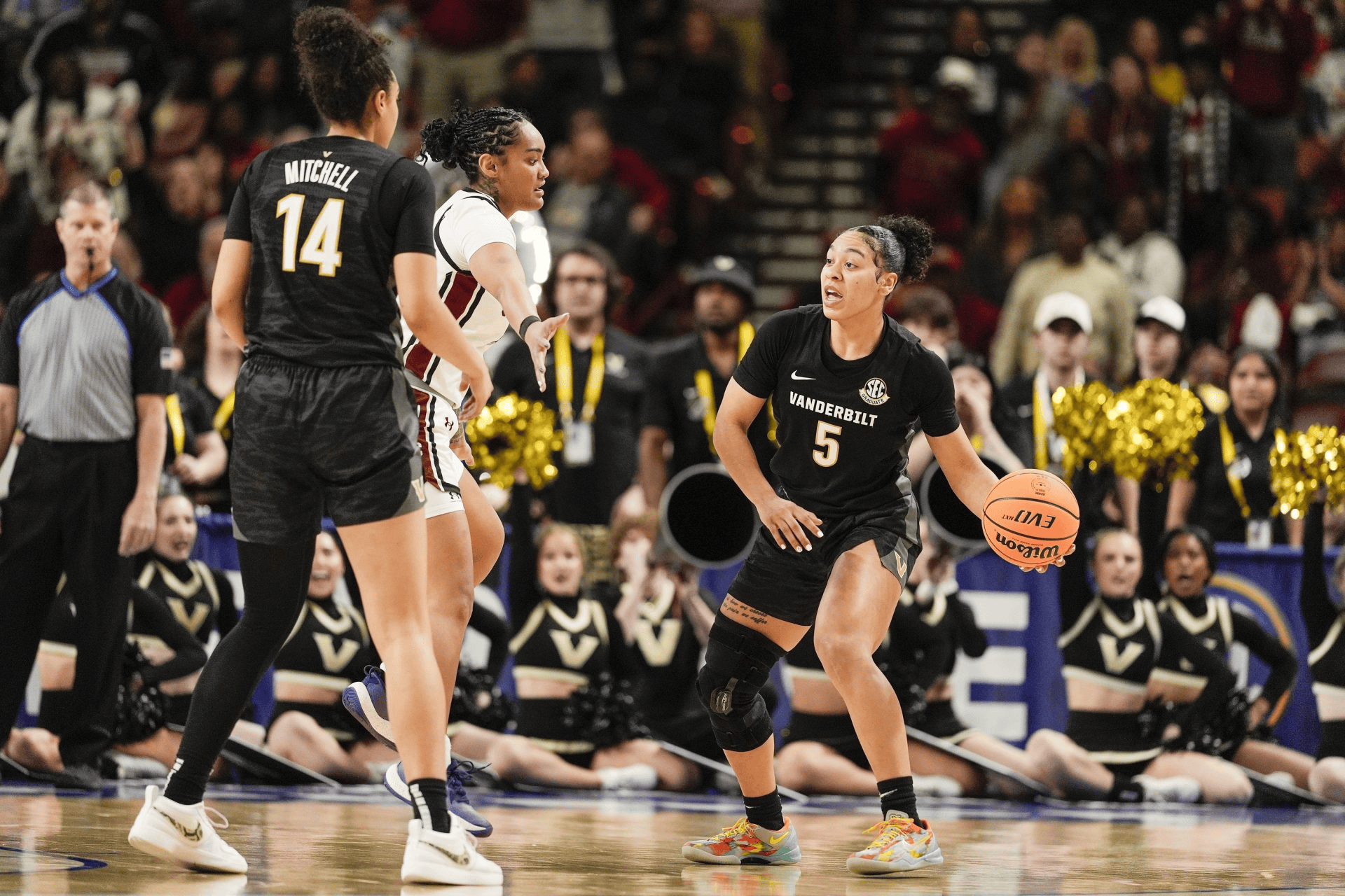 A Vanderbilt basketball player dribbles the ball on the court, looking towards another player from an opposing team, during a game.