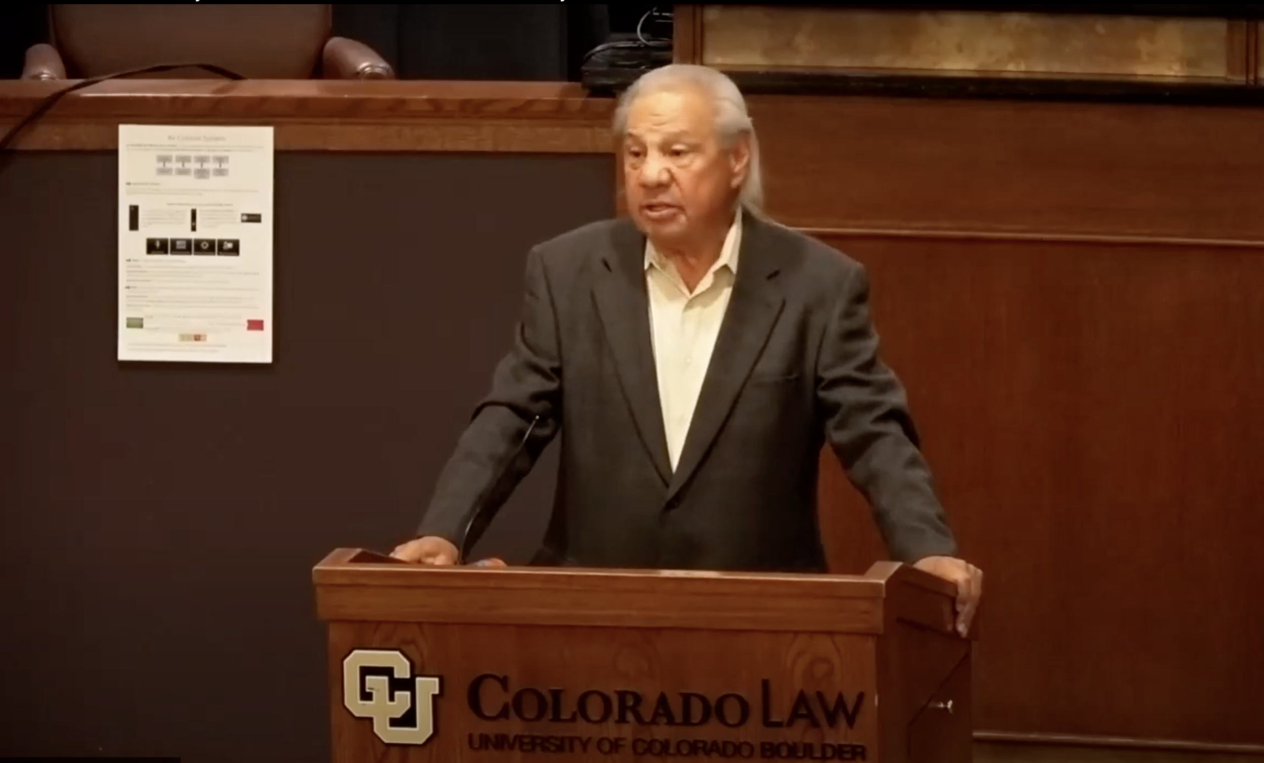 Man speaking behind podium during panel discussion on the native American experience.