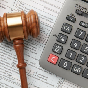A high-angle close-up of a judge's gavel and a calculator resting on tax forms, symbolizing legal or financial matters.