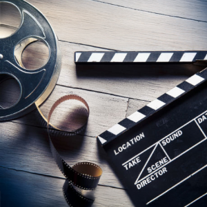 A top-down view of a film reel with unspooled film and an open clapperboard on a wooden surface, suggesting filmmaking or media production.