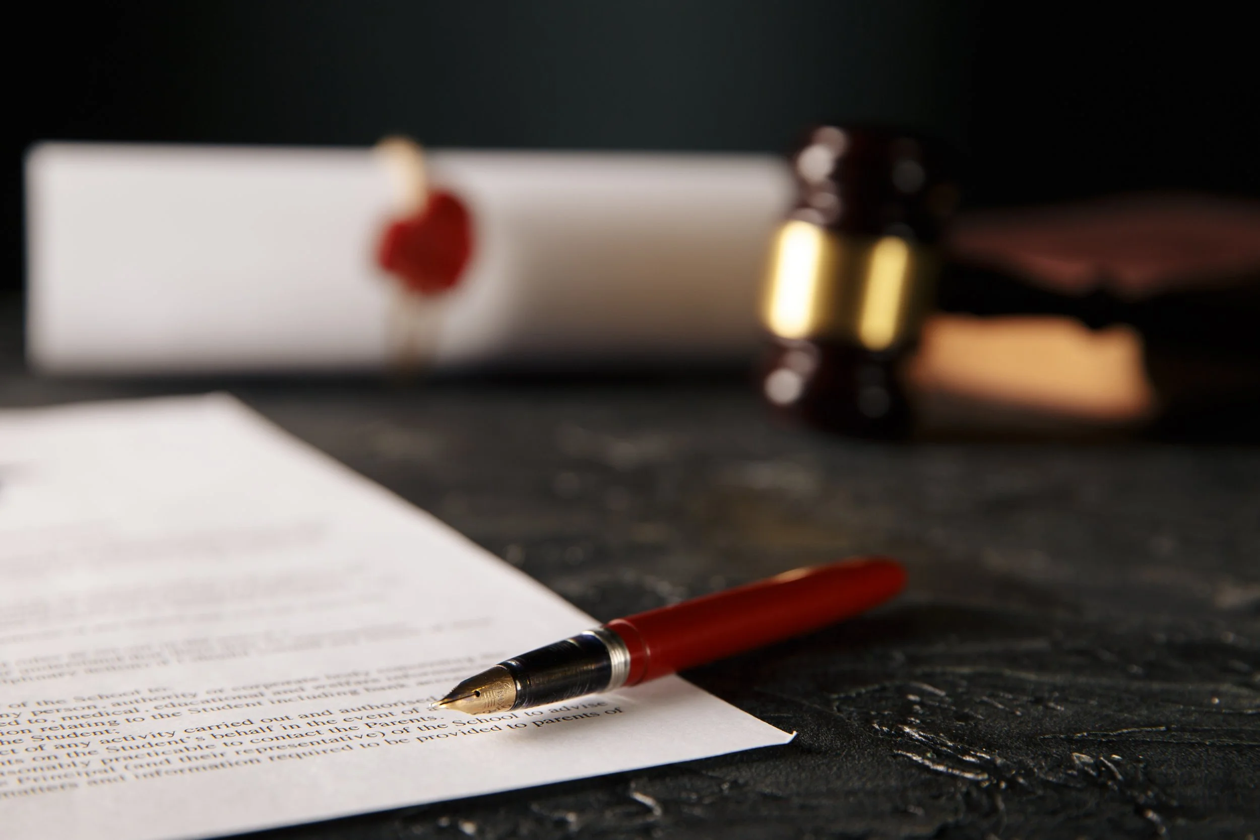 Fountain pen on top of printed document, with gavel and rolled document out of focus in the background
