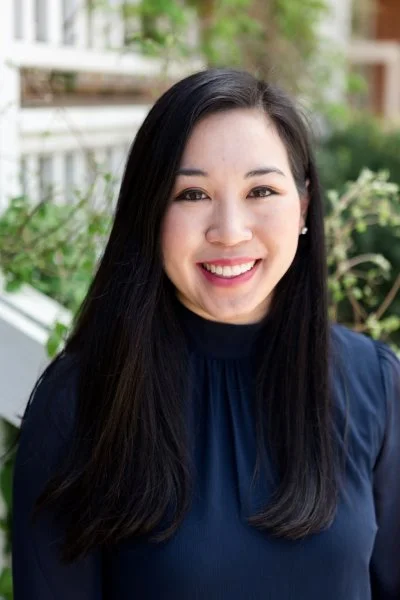 A close-up headshot of a smiling woman with long, dark hair.