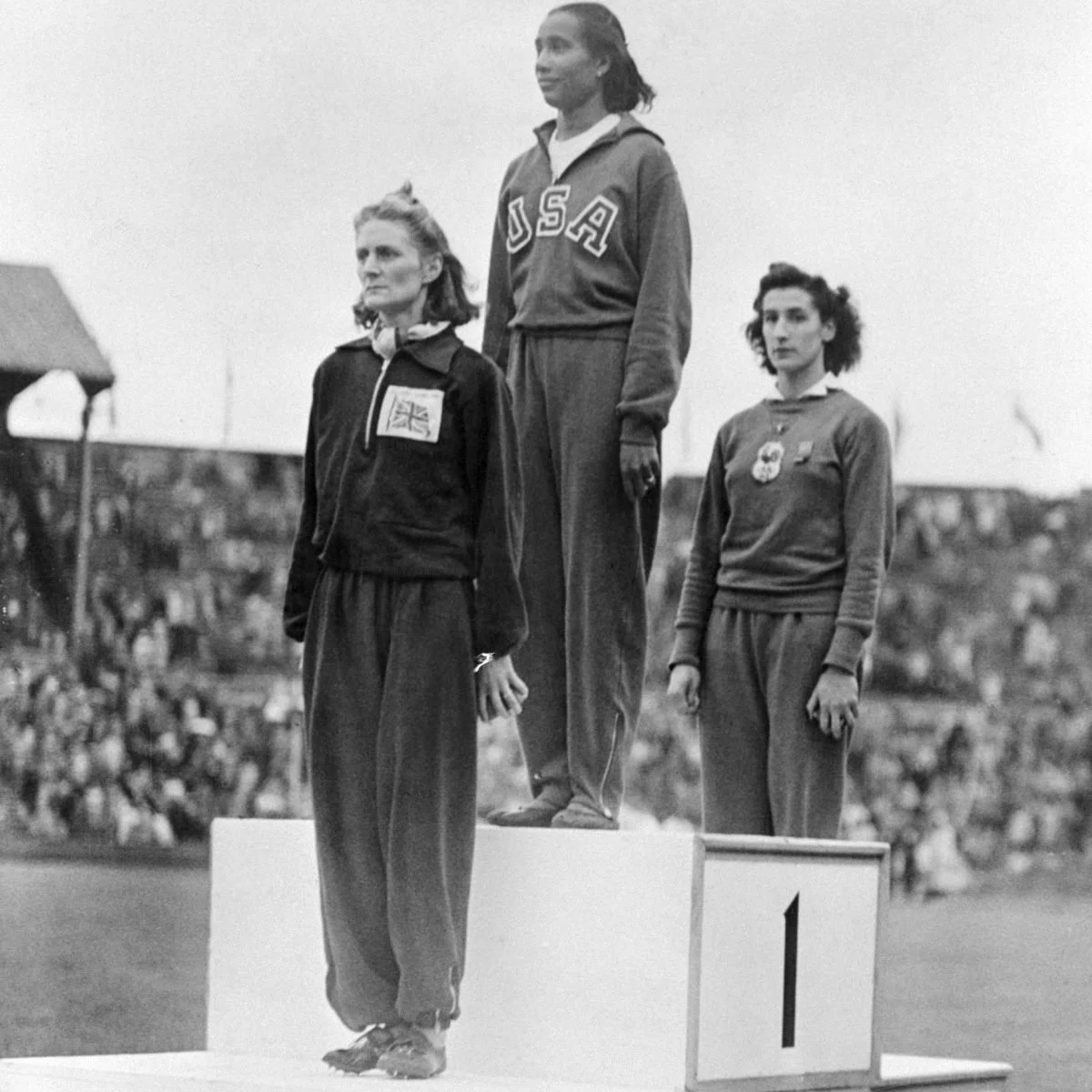 A black and white photo of Alice Coachman on a podium, standing above the other competitors.