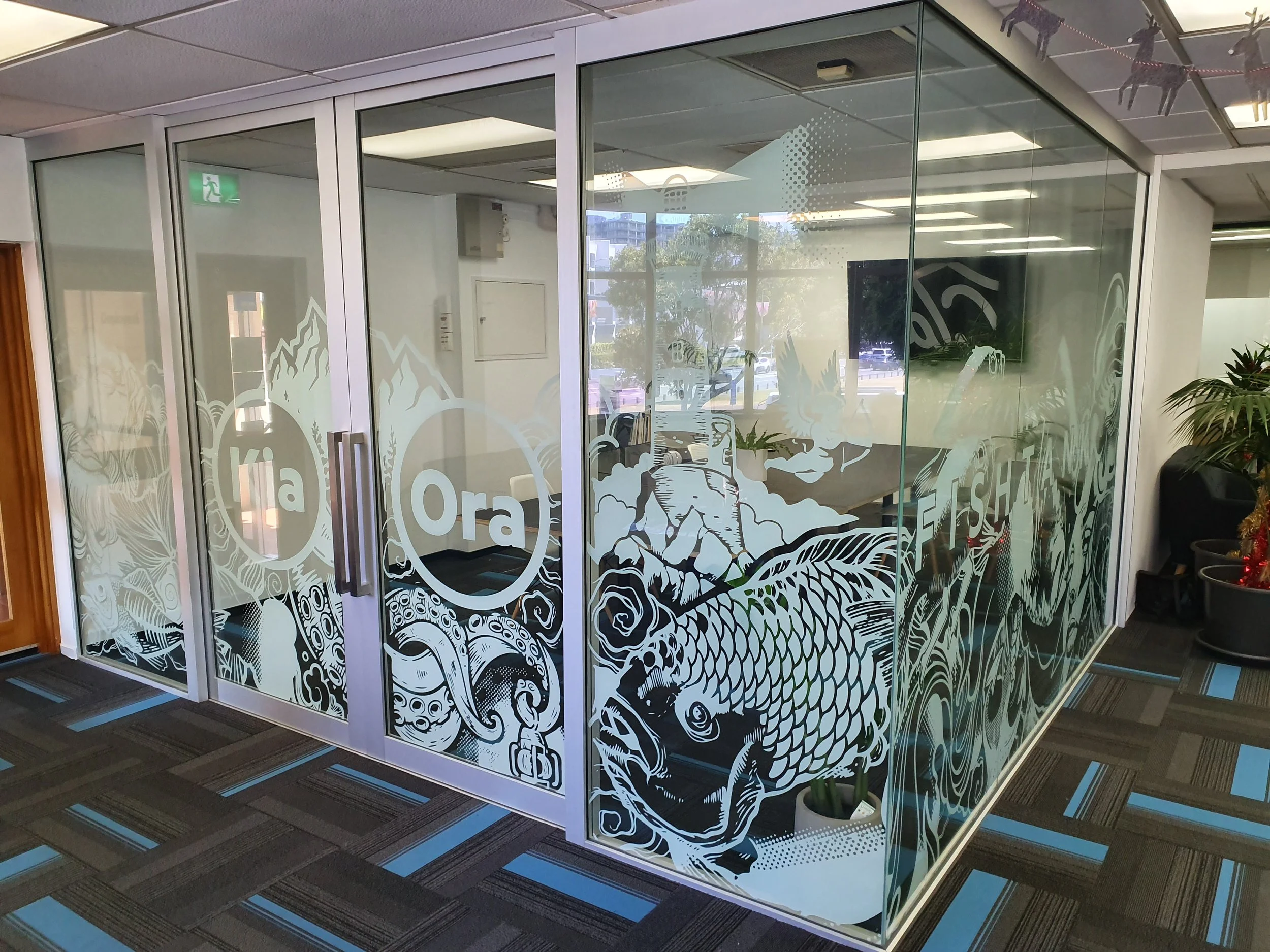 Glass office partition with Chinese dragon and ocean wave illustrations, and the text 'ia Ora' printed on the glass panels.