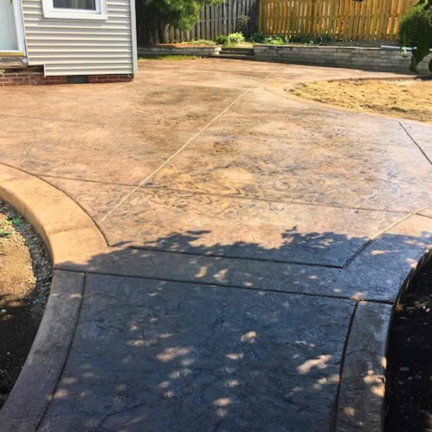 Concrete patio with curved edge and garden bed with plants in a backyard.