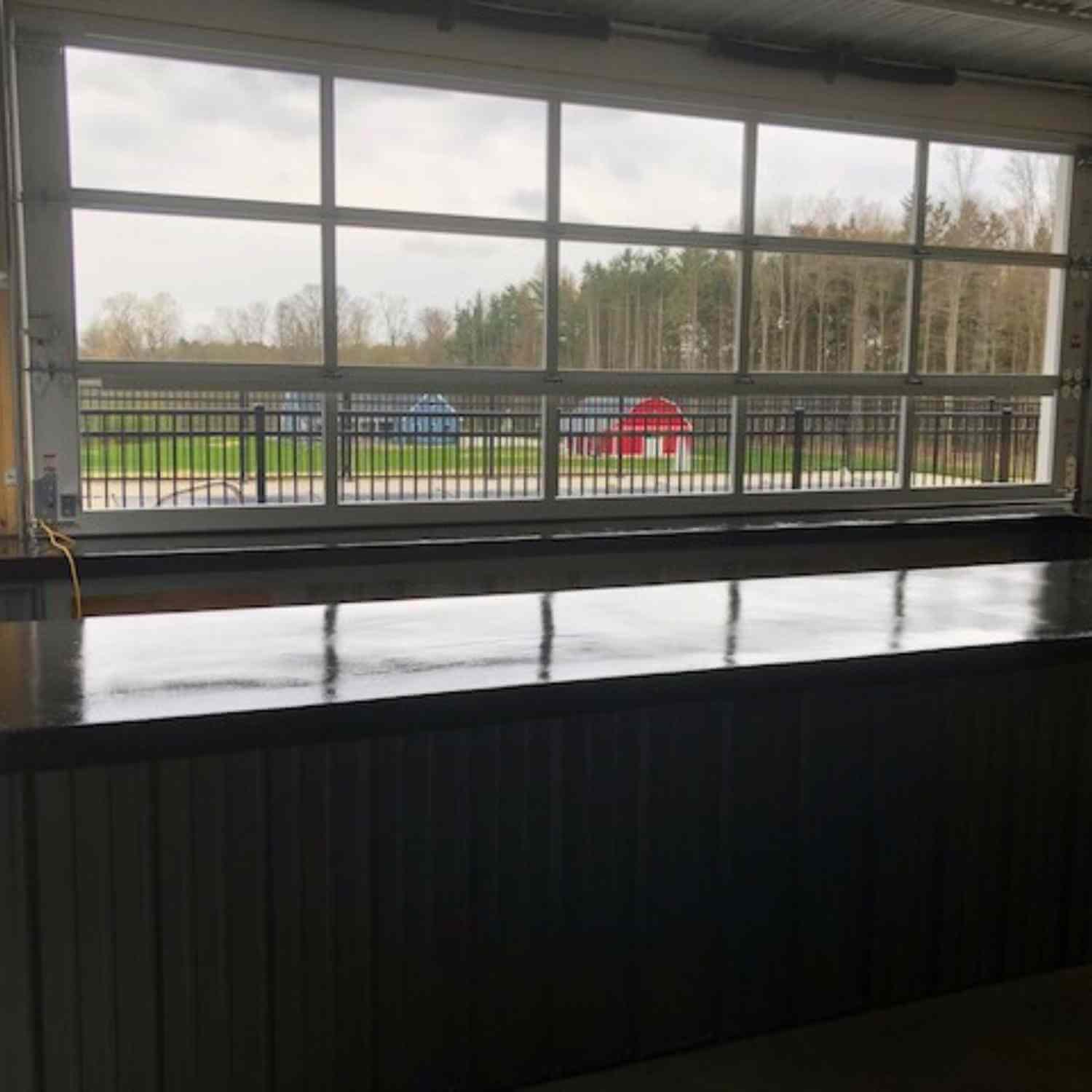 Garage interior with a black concrete counter and a large window showing a grassy field with two red and blue structures outside.