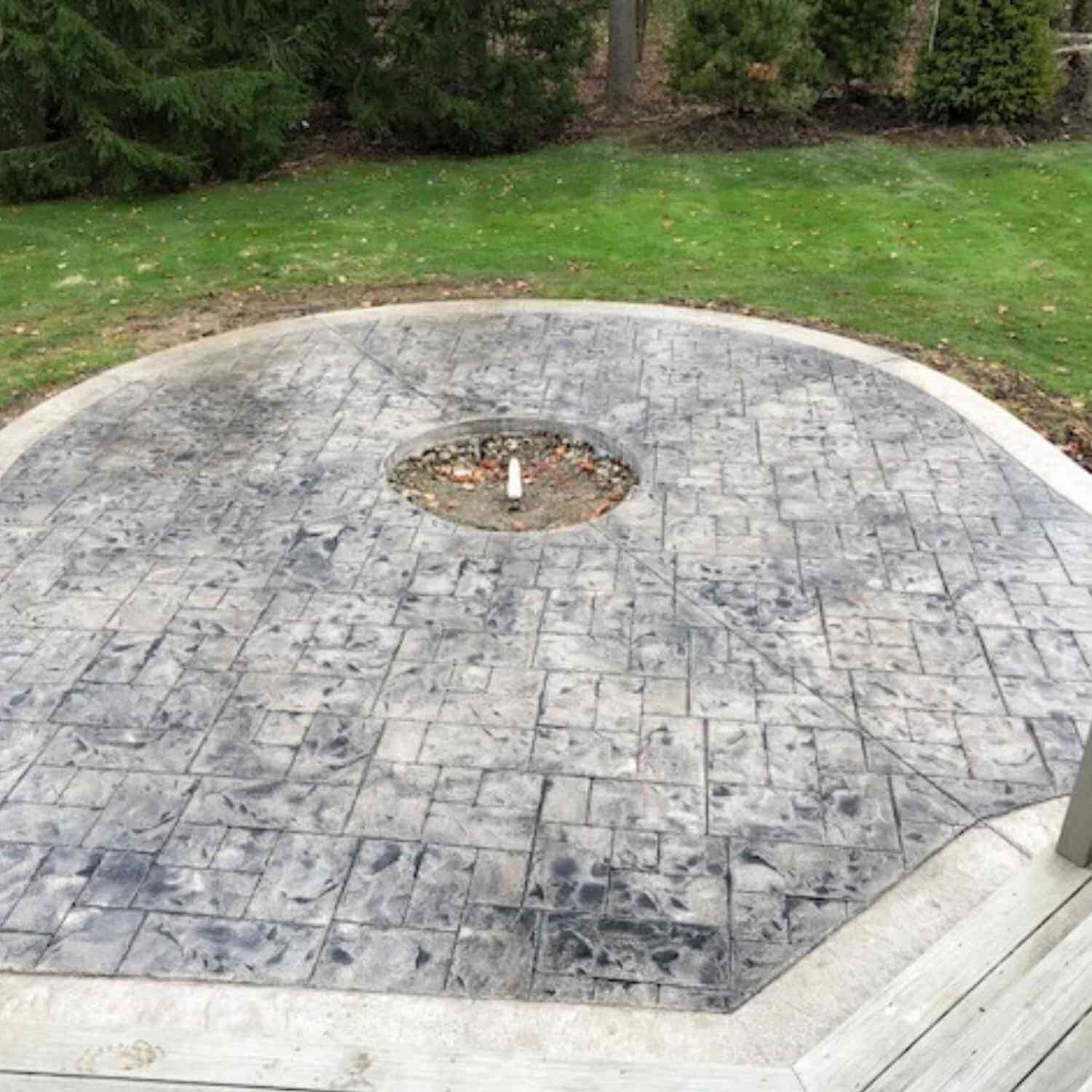 Backyard patio in Ohio with gray stone stamped concrete and a small circular fire pit area in the center, surrounded by grass and trees.