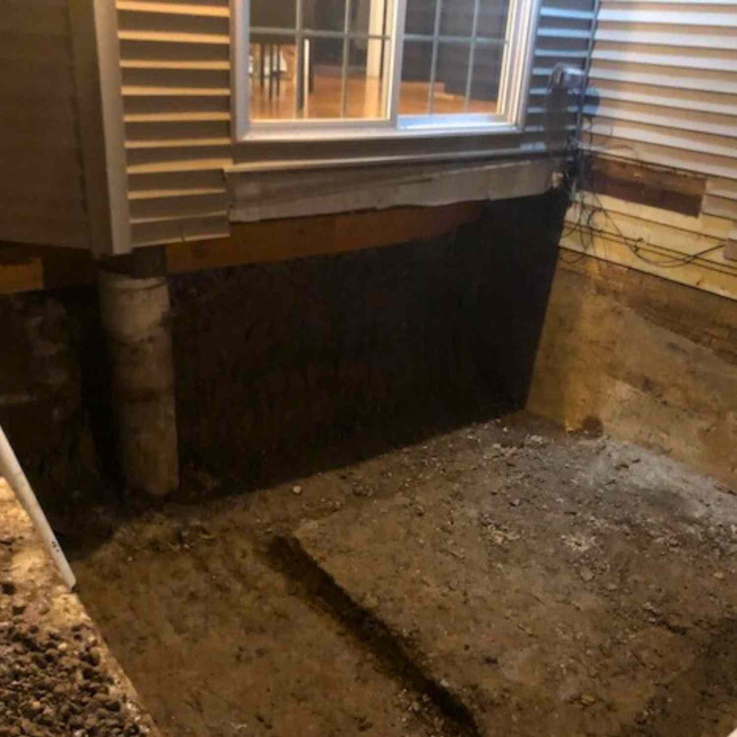 Basement foundation repair in Euclid, Ohio in progress with exposed soil, concrete footing, and black waterproofing membrane under a porch.