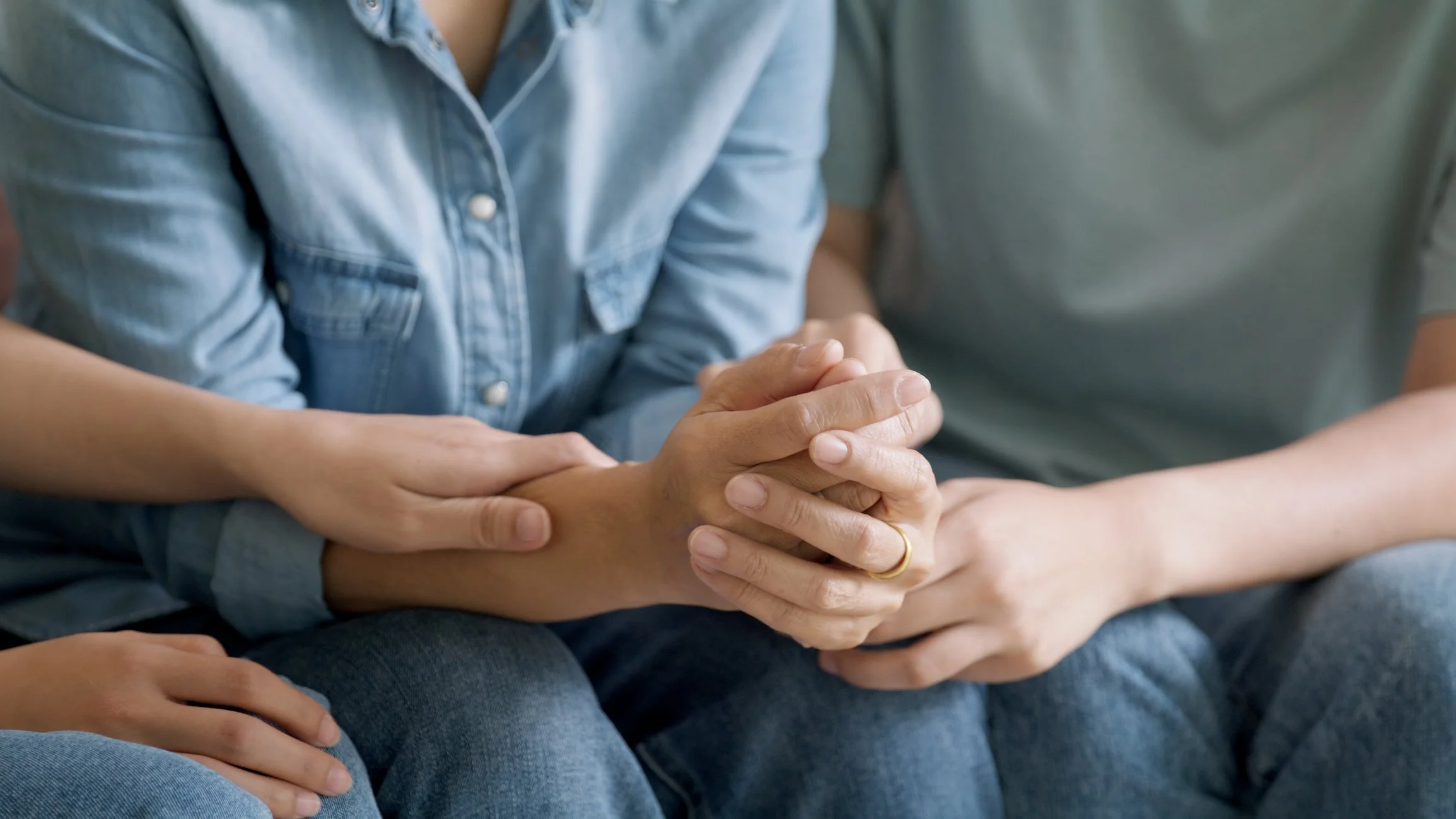 Close-up of two people holding hands, one with a gold ring, sitting close together.