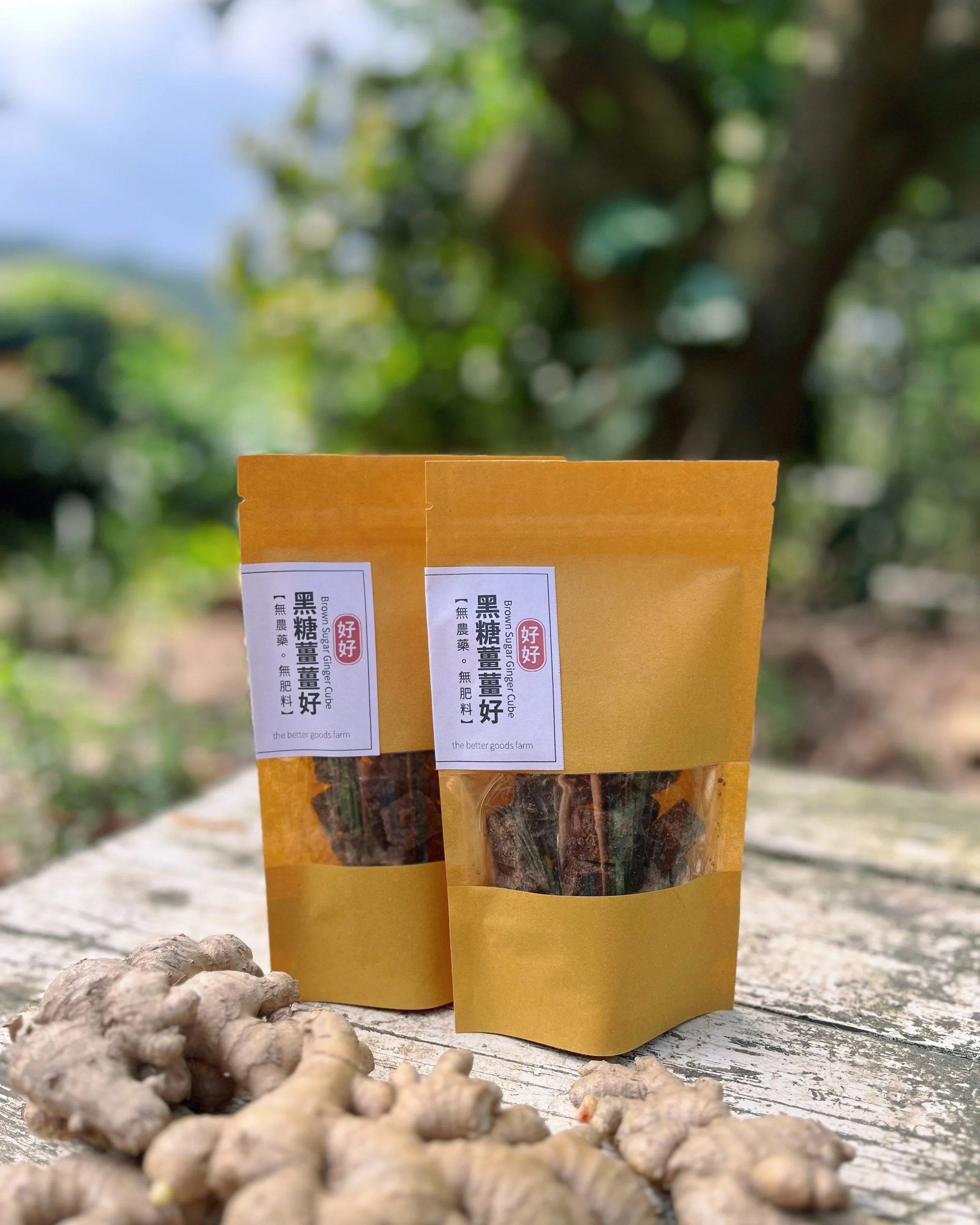 Brown paper bags labeled with Chinese text, containing dried goods, placed on a wooden surface with fresh ginger in the foreground, in an outdoor setting with greenery.
