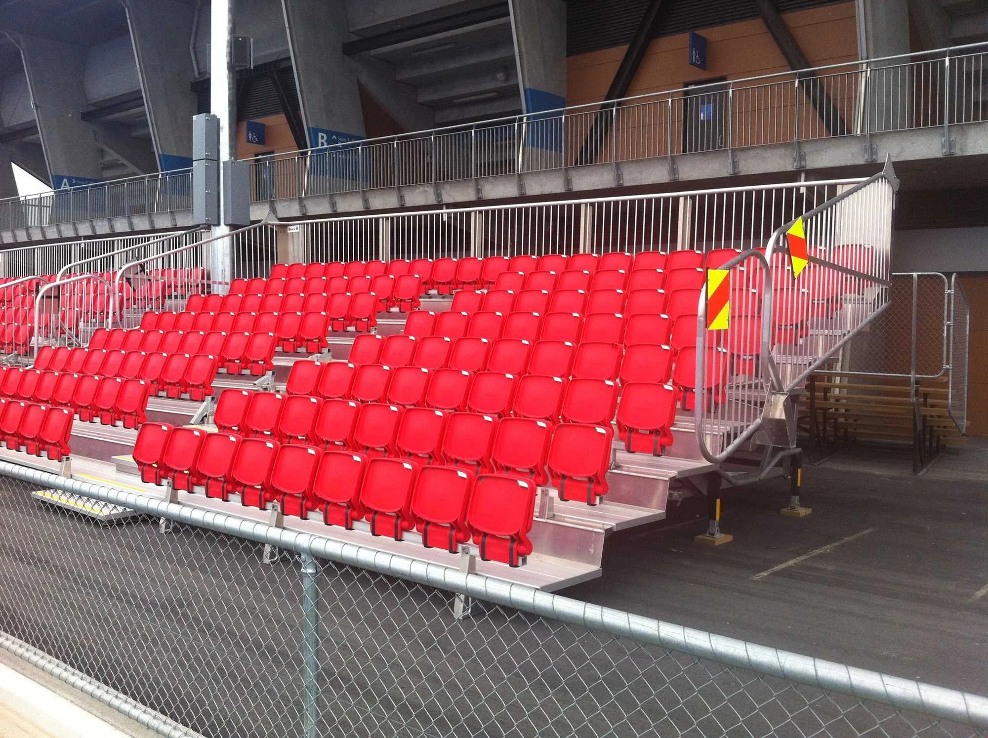 Empty red stadium seats with a metal staircase and safety railings in an indoor arena.
