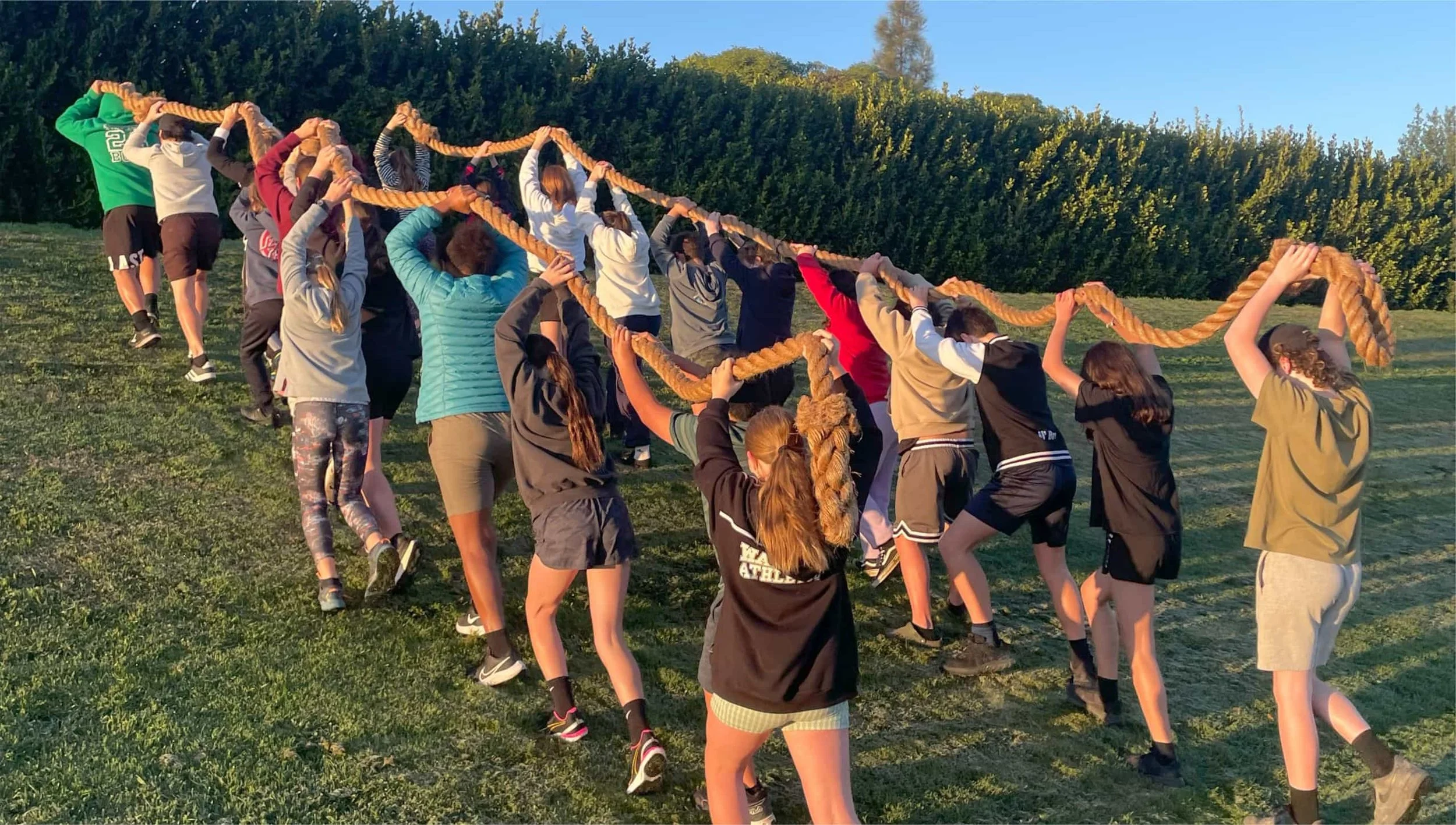 Group of children participating in an outdoor tug-of-war game with a thick rope on a grassy field during daytime.