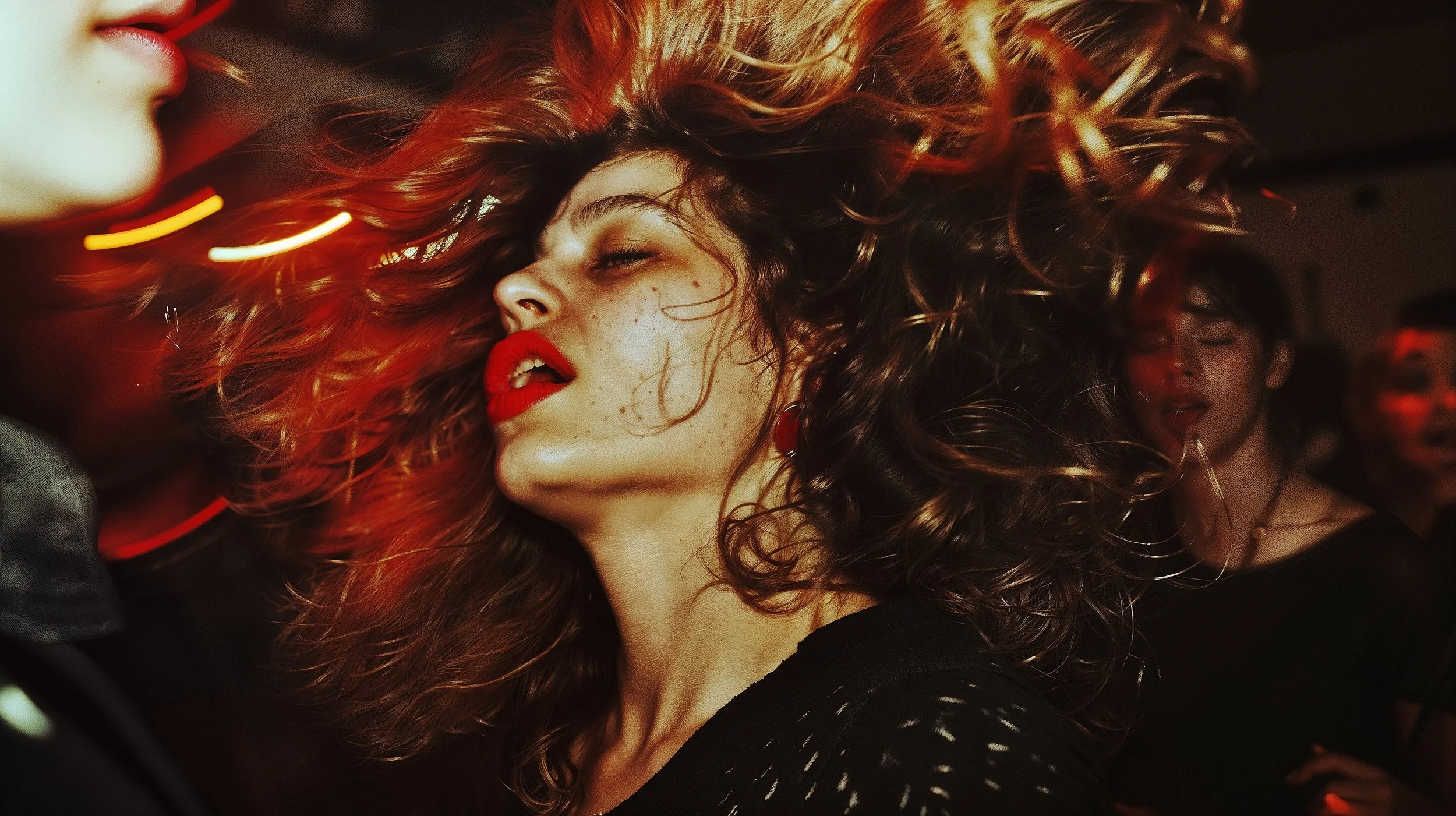 A woman with curly hair, red lipstick, and freckles dancing at a party with others in the background, some with eyes closed and smiling.