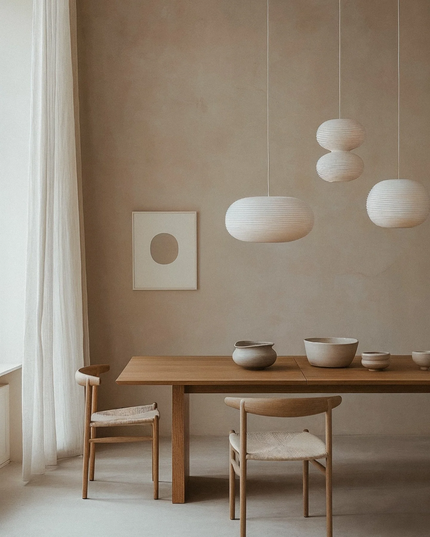 Minimalist dining room with wooden table, two chairs, hanging white pendant lights, and neutral decor.