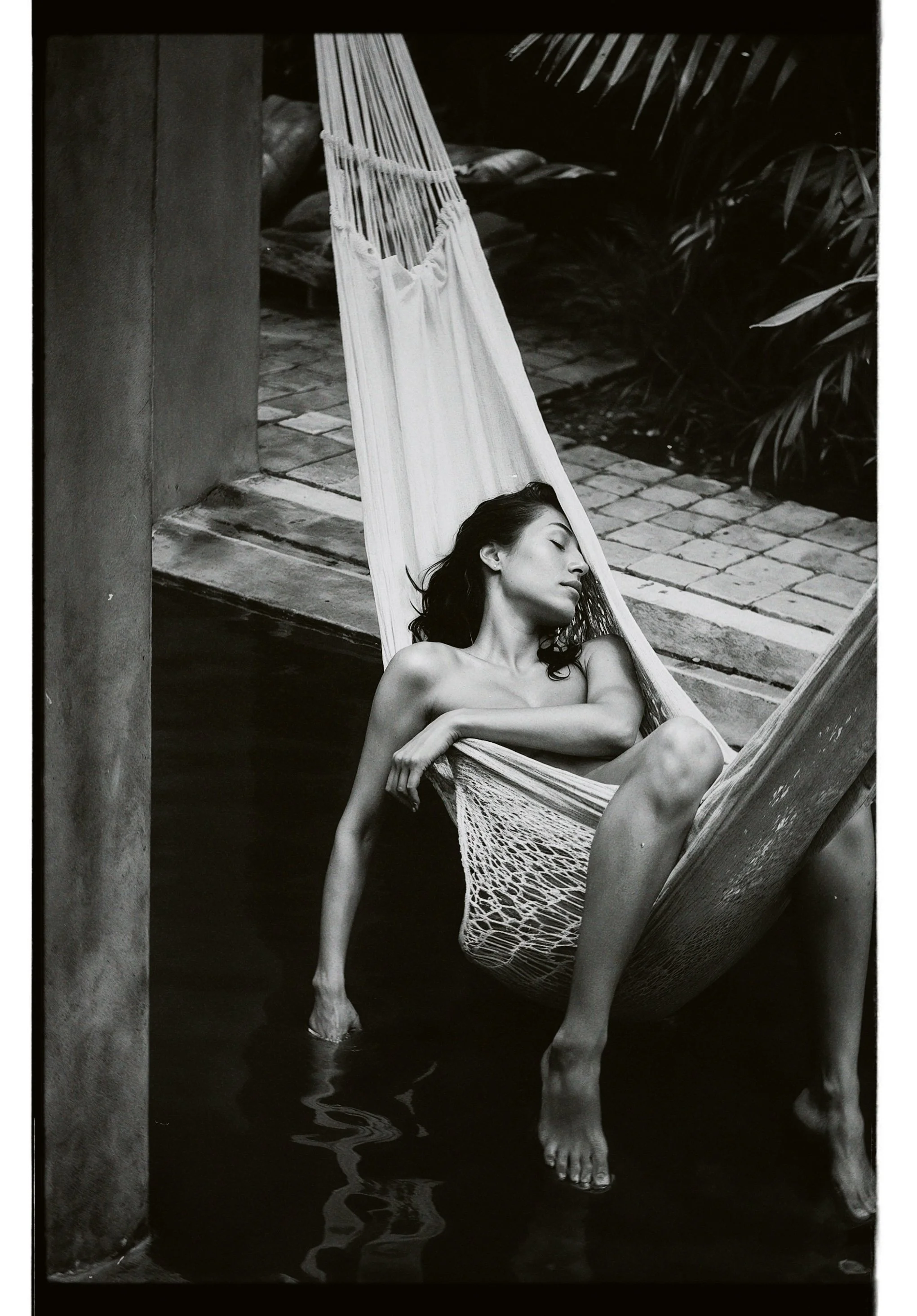 A woman resting in a hammock with her eyes closed and arms crossed, partially submerged in water.