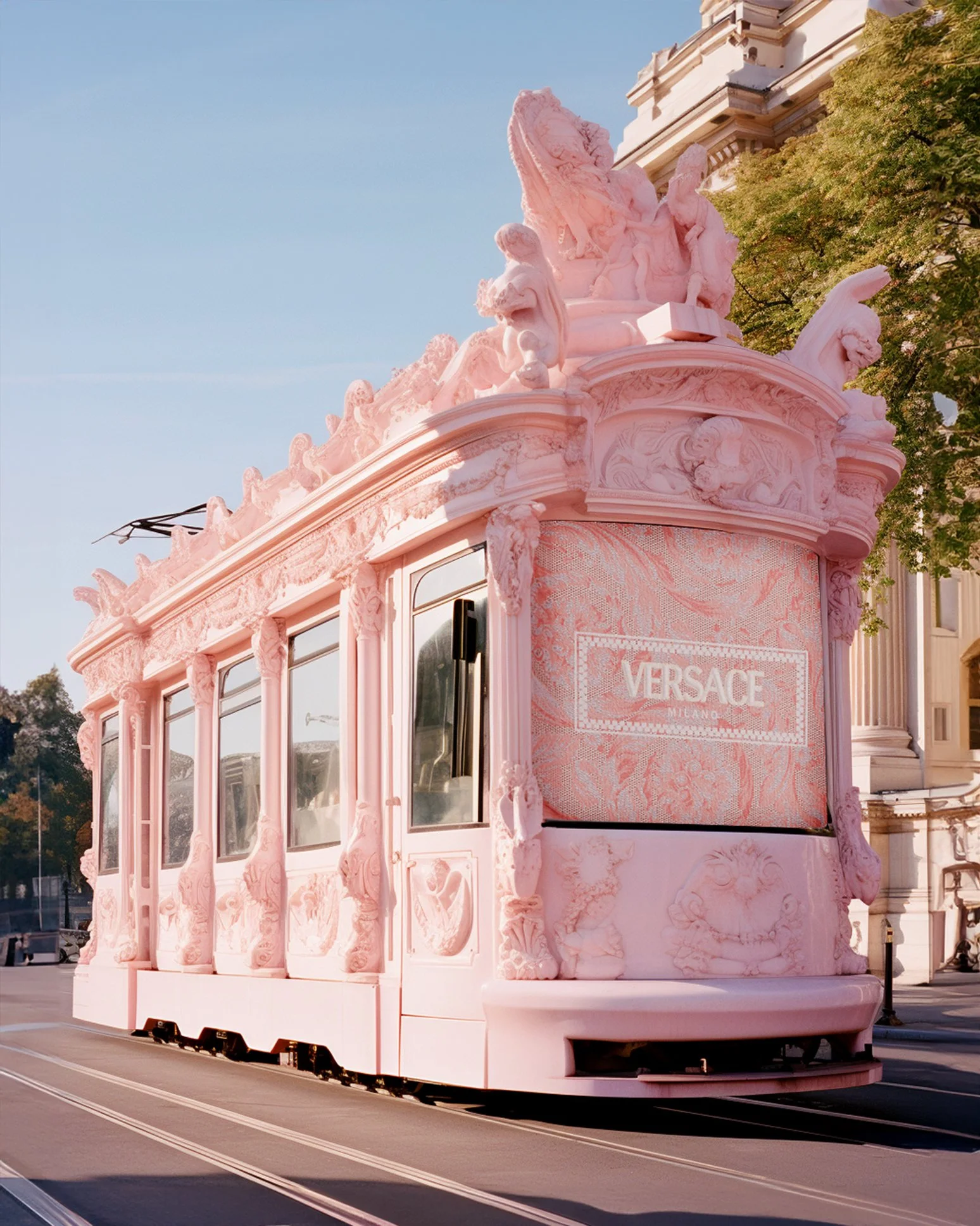 Pink Versace-branded tram decorated with ornate sculptures and carvings, traveling on street rails in an urban area.