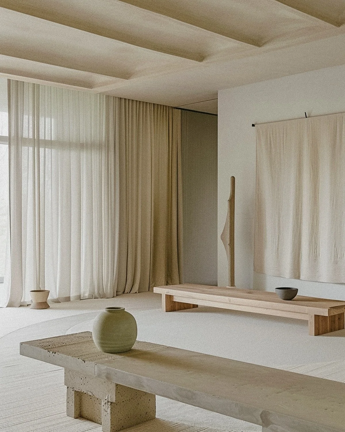 Minimalist interior with neutral tones, wooden benches, ceramic vases, and large sheer curtains.