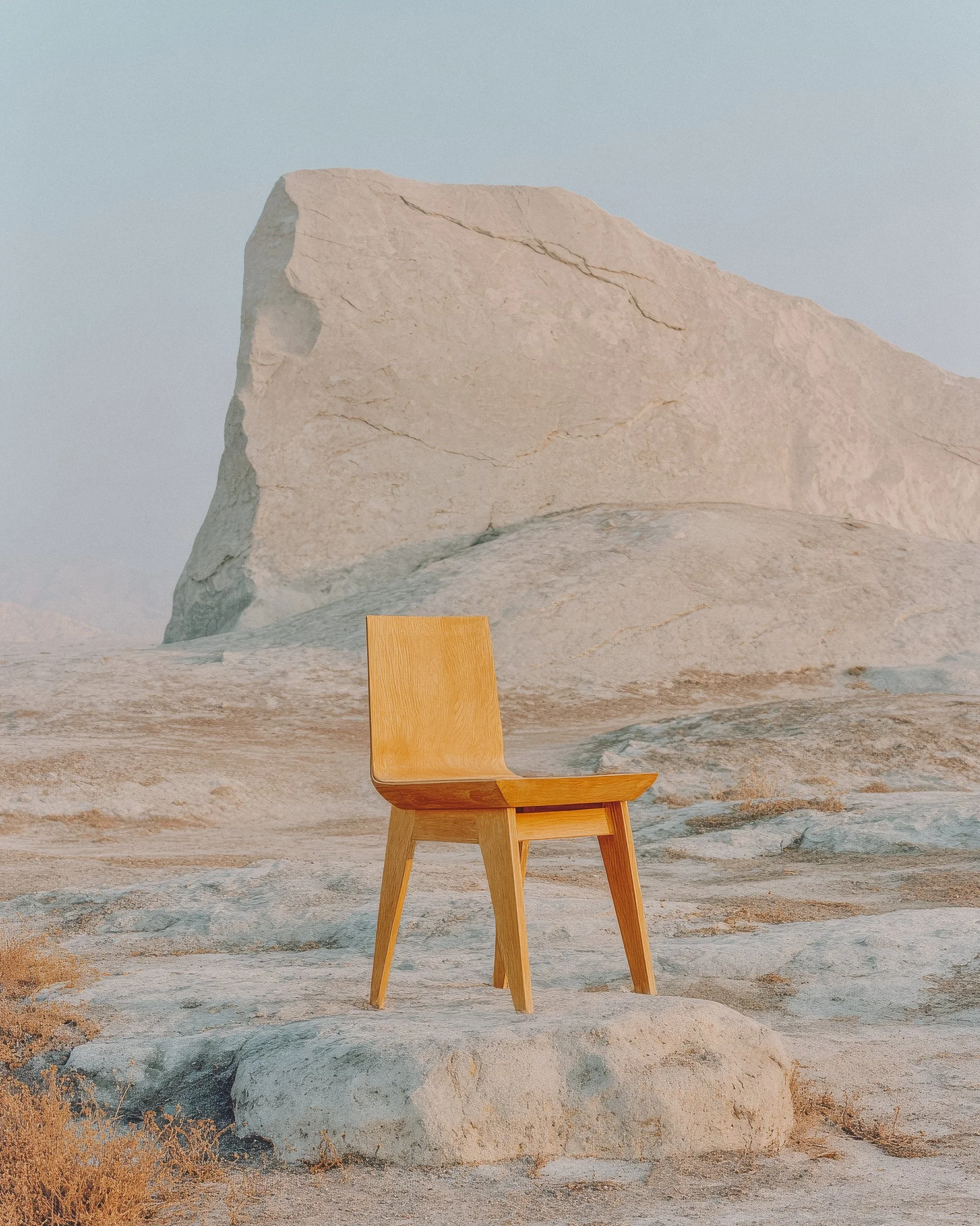 A wooden chair on a rocky desert landscape with large rock formations in the background.