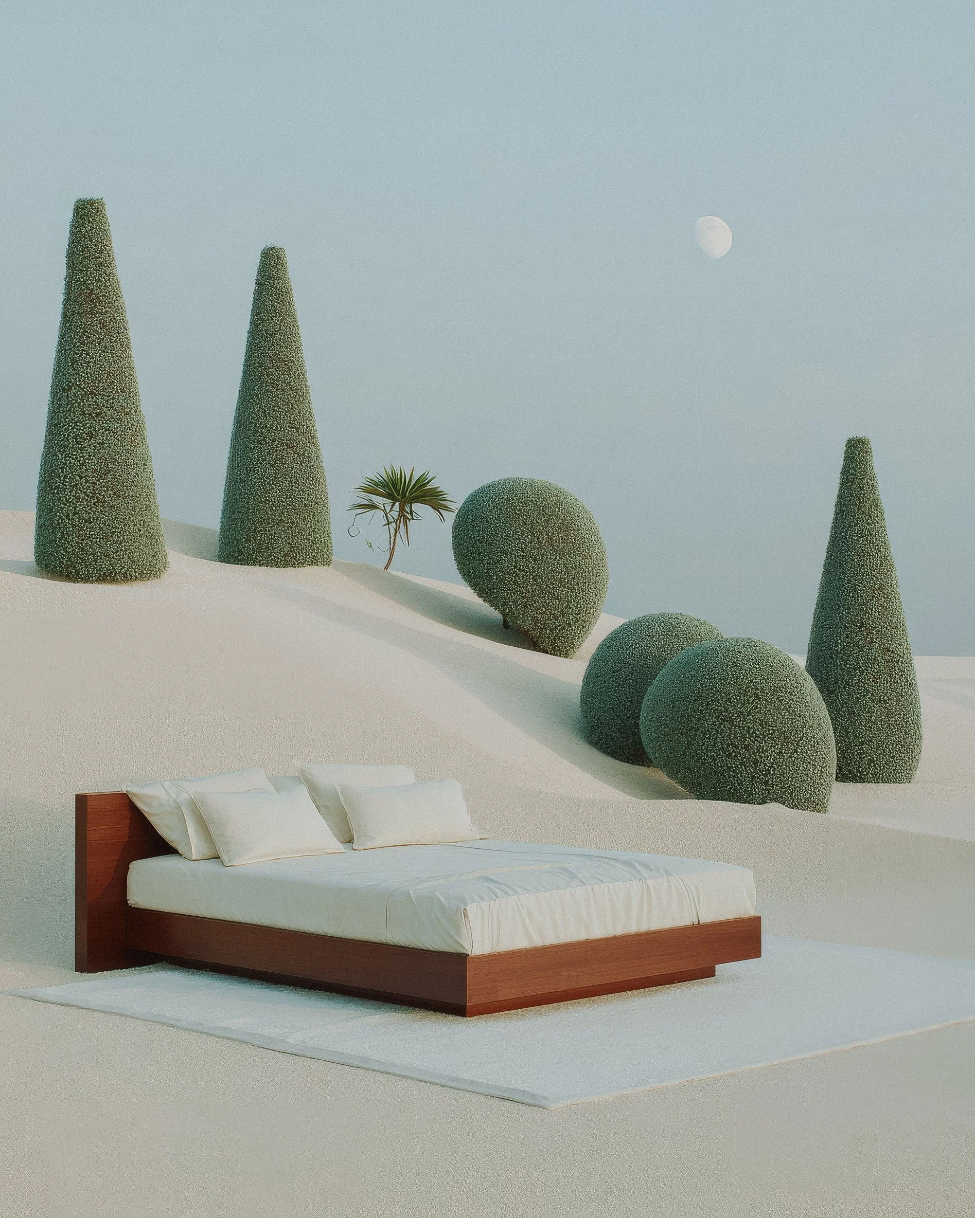 A bed with white bedding and pillows on a white rug, outdoors on a sand dune with green, cone-shaped, and spherical bushes and trees in the background under a pale sky with the moon visible.