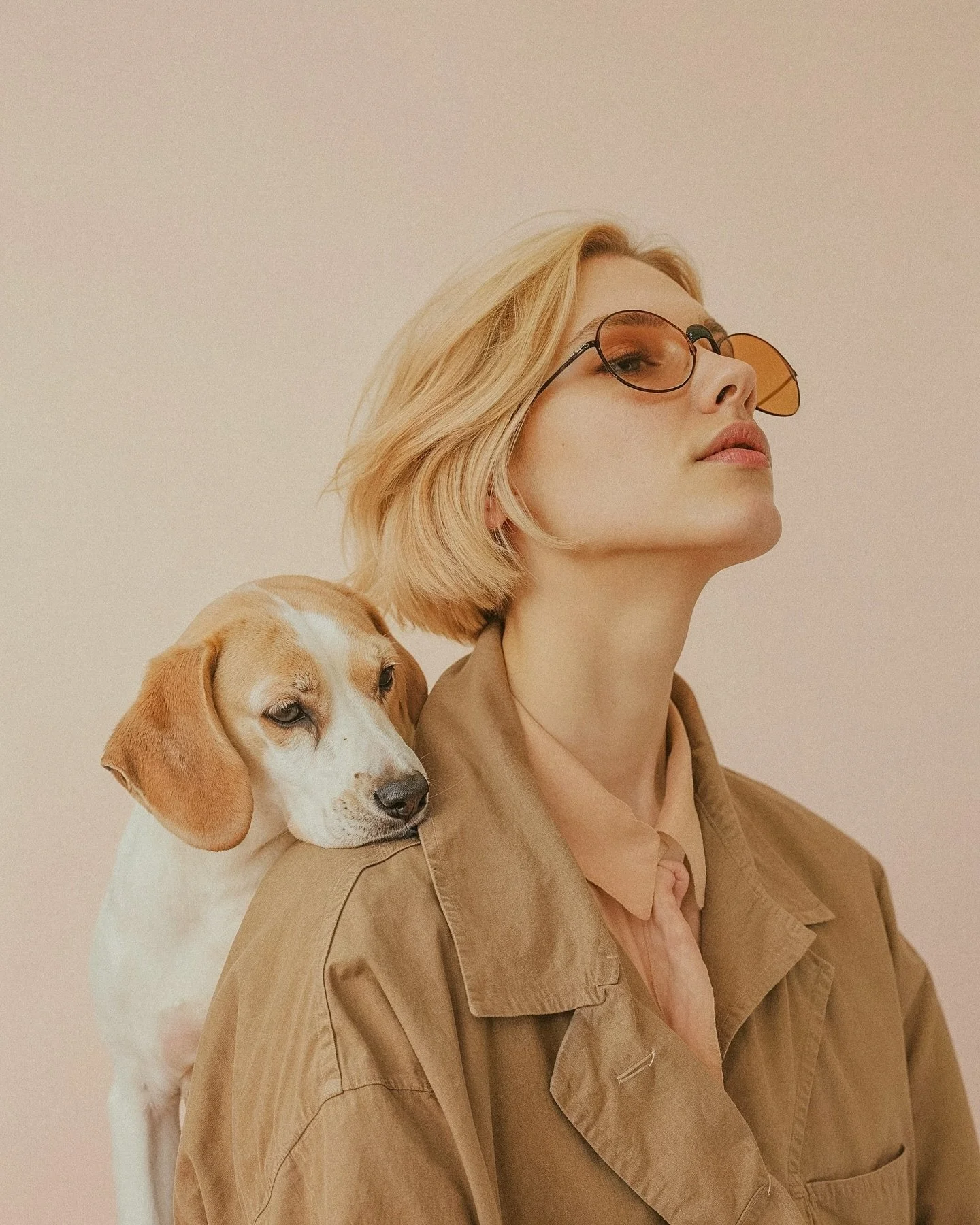 A young woman with blonde hair wearing sunglasses and a brown jacket, with a small dog resting its head on her shoulder.