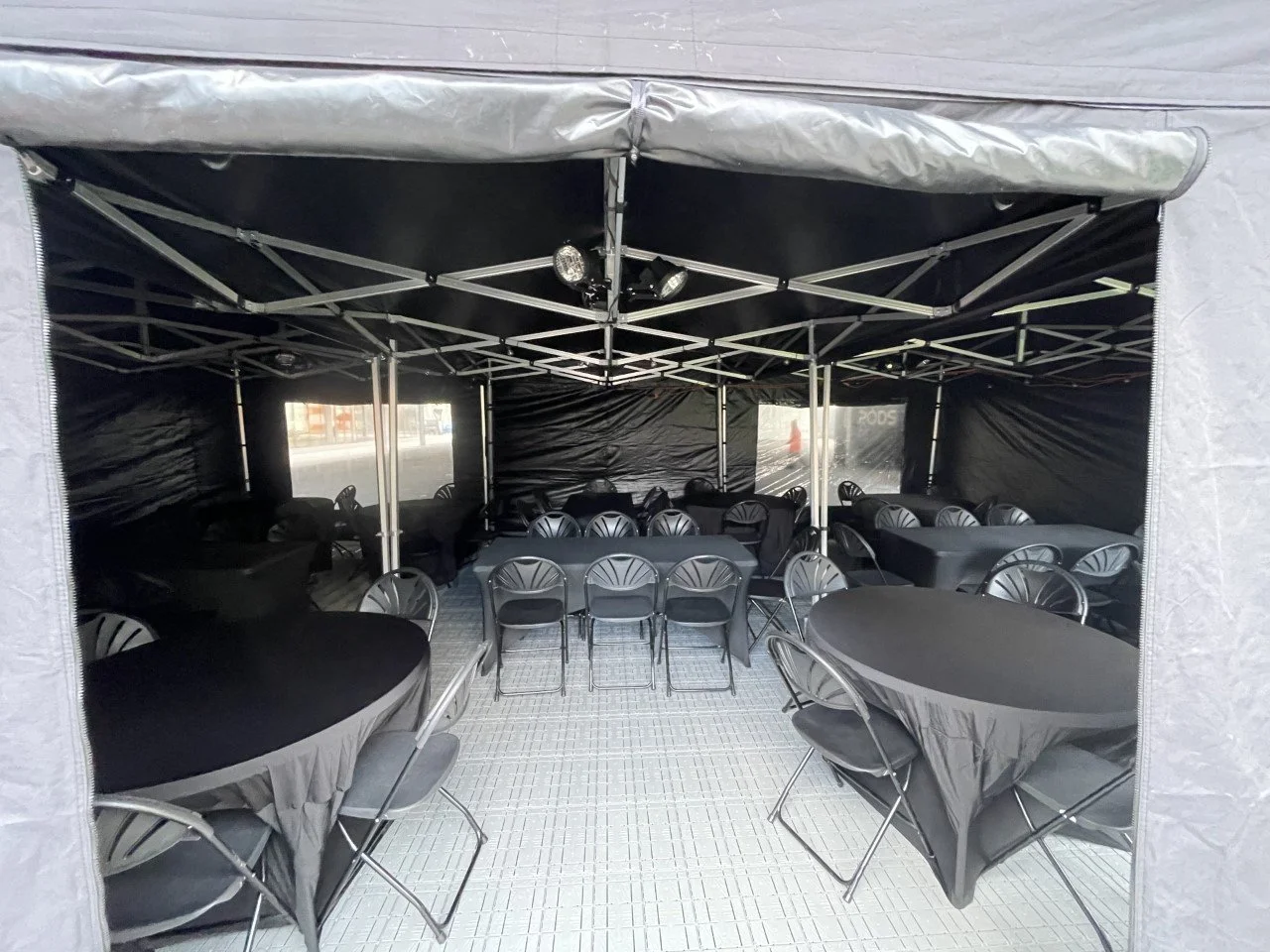 Setup of a large black event tent with tables and chairs inside.