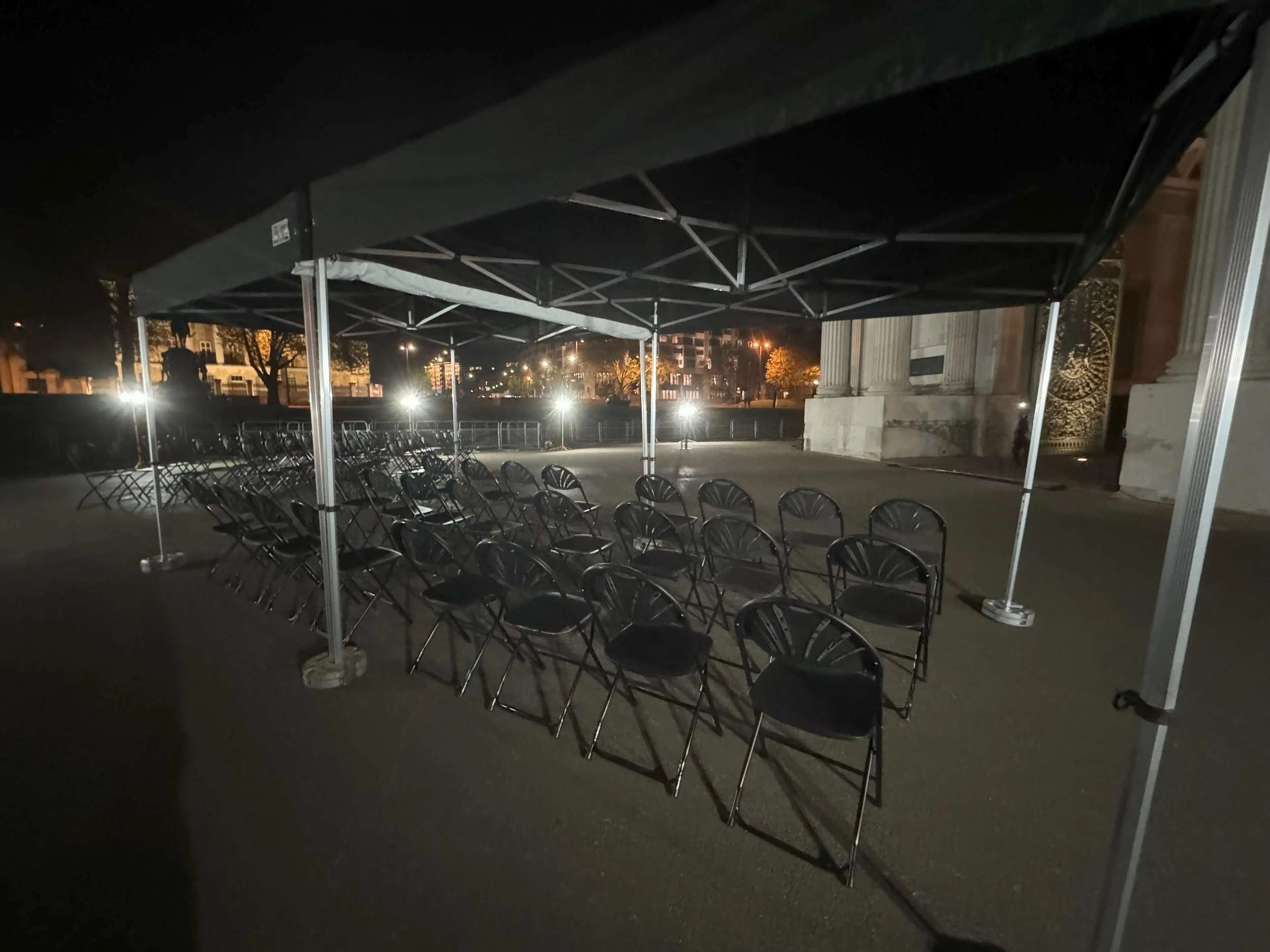 Empty metal chairs under a black canopy tent outdoors at night, with bright streetlights and a historic building in the background. marquee hire
gazebo hire
party tent hire
party marquee hire
event tent hire
wedding marquee hire
pop up gazebo hire
co