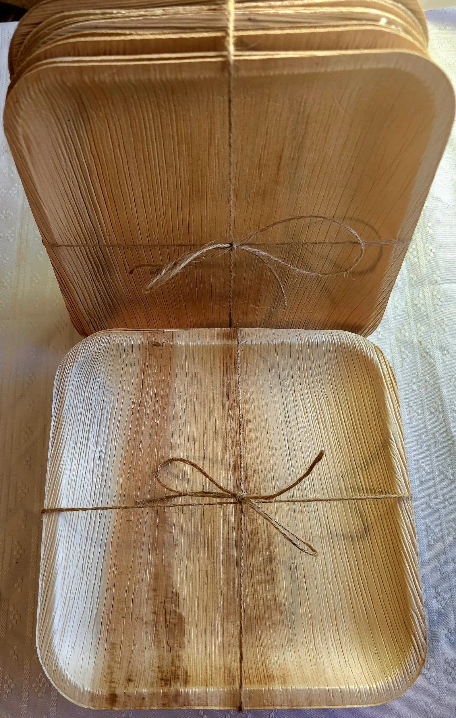 Two square wooden trays wrapped with string tied in a bow, placed on a textured tablecloth.