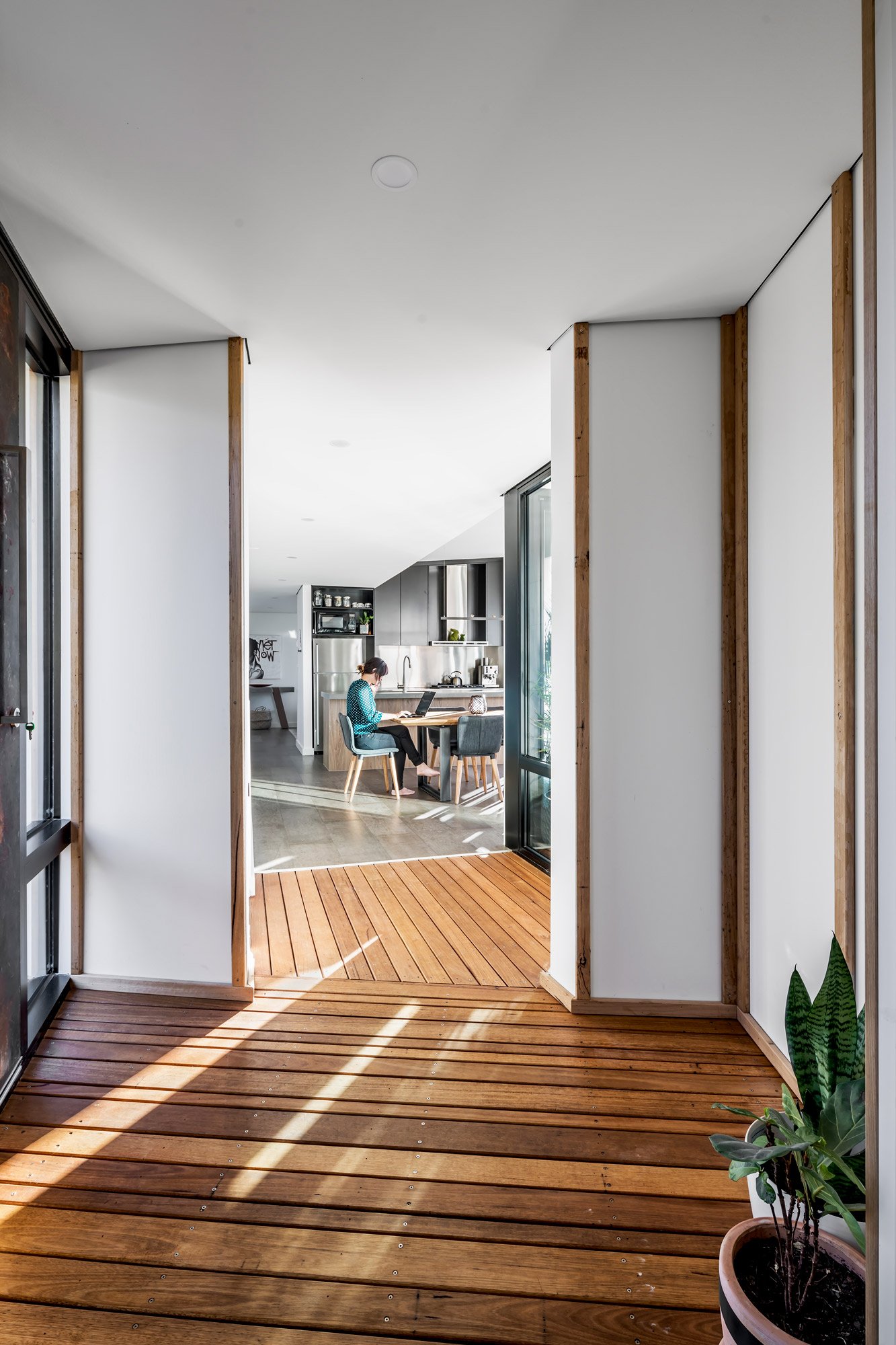 An interior perspective looking down a hallway into an open-plan dining area. The view emphasizes the home's layout and spatial flow, leading the eye from the narrow corridor into the bright, airy living space.