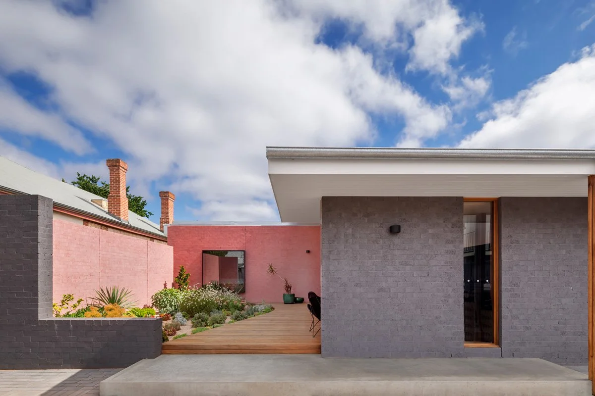 Grey bungalow style house and pink facade framing the timber deck and landscaping.
