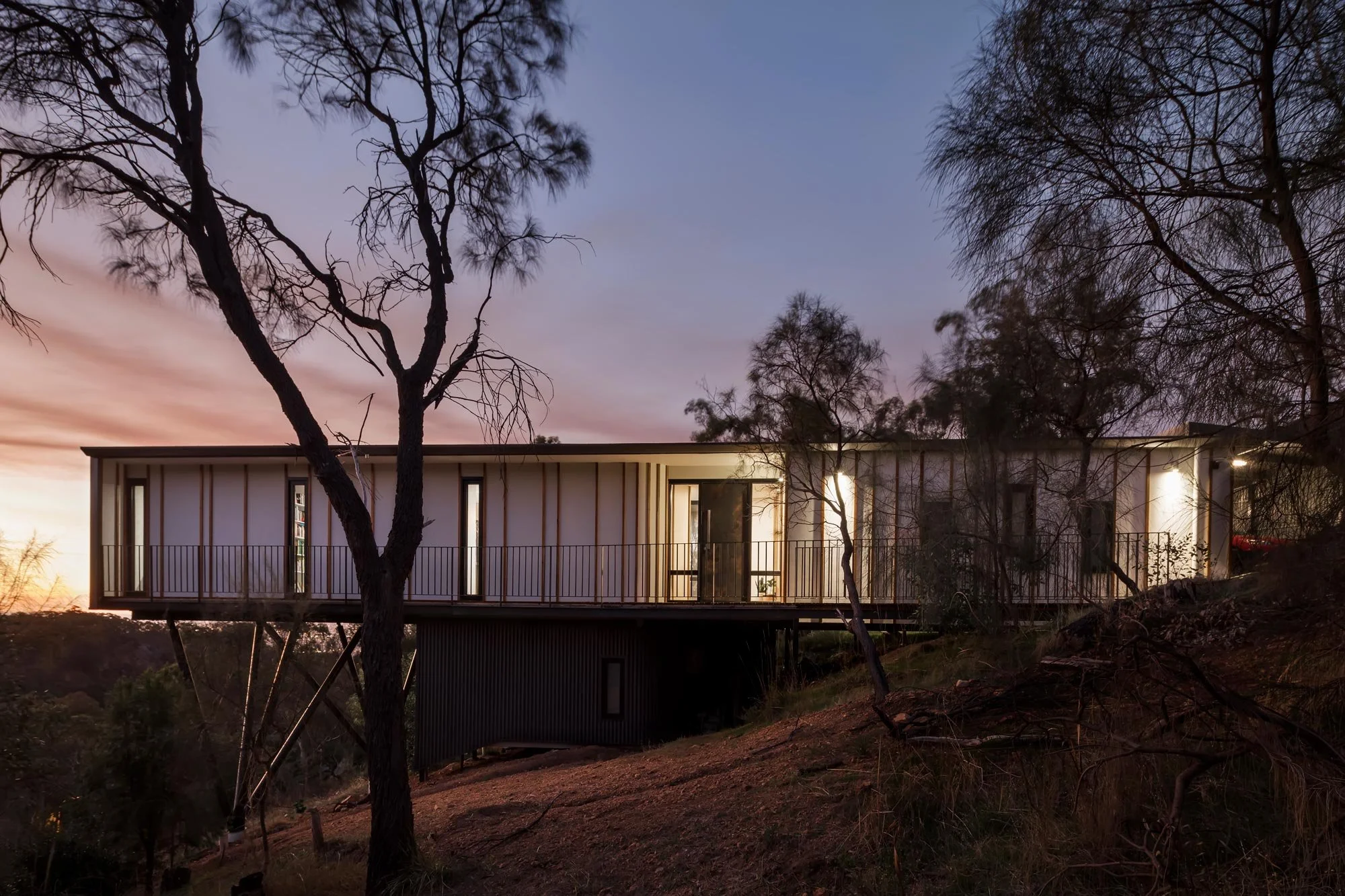 Rear view of a box shaped white house surrounded by trees