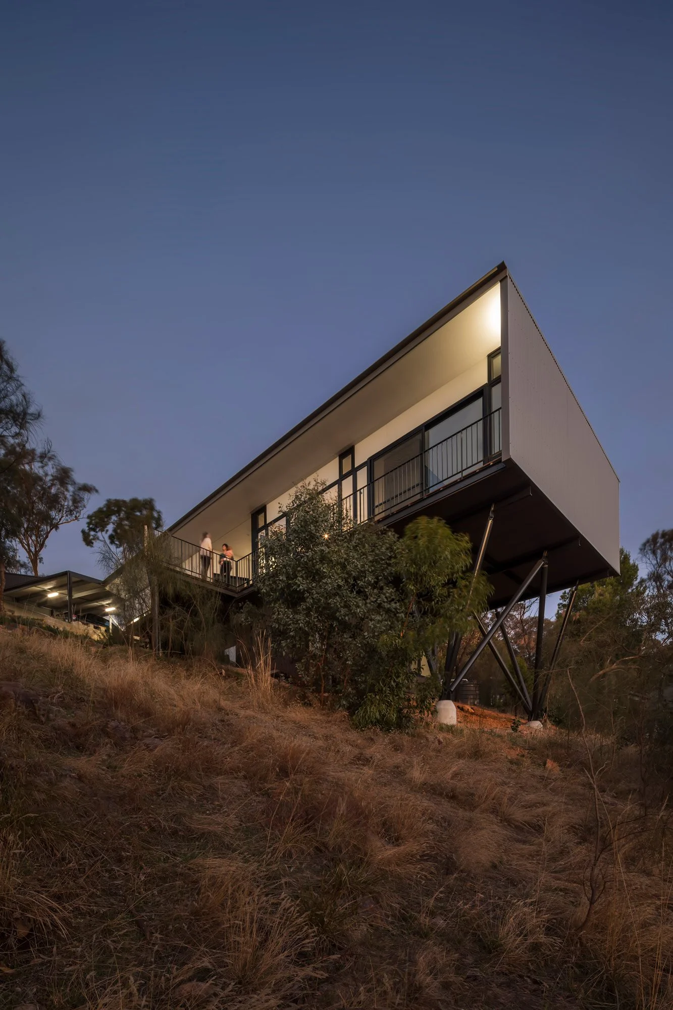 Upward view onto the house on stilts, ephasising its dramatic overhand across the hill and exposing the stilts that were purposfully used to minimise architectural footprint in the Australian bush.
