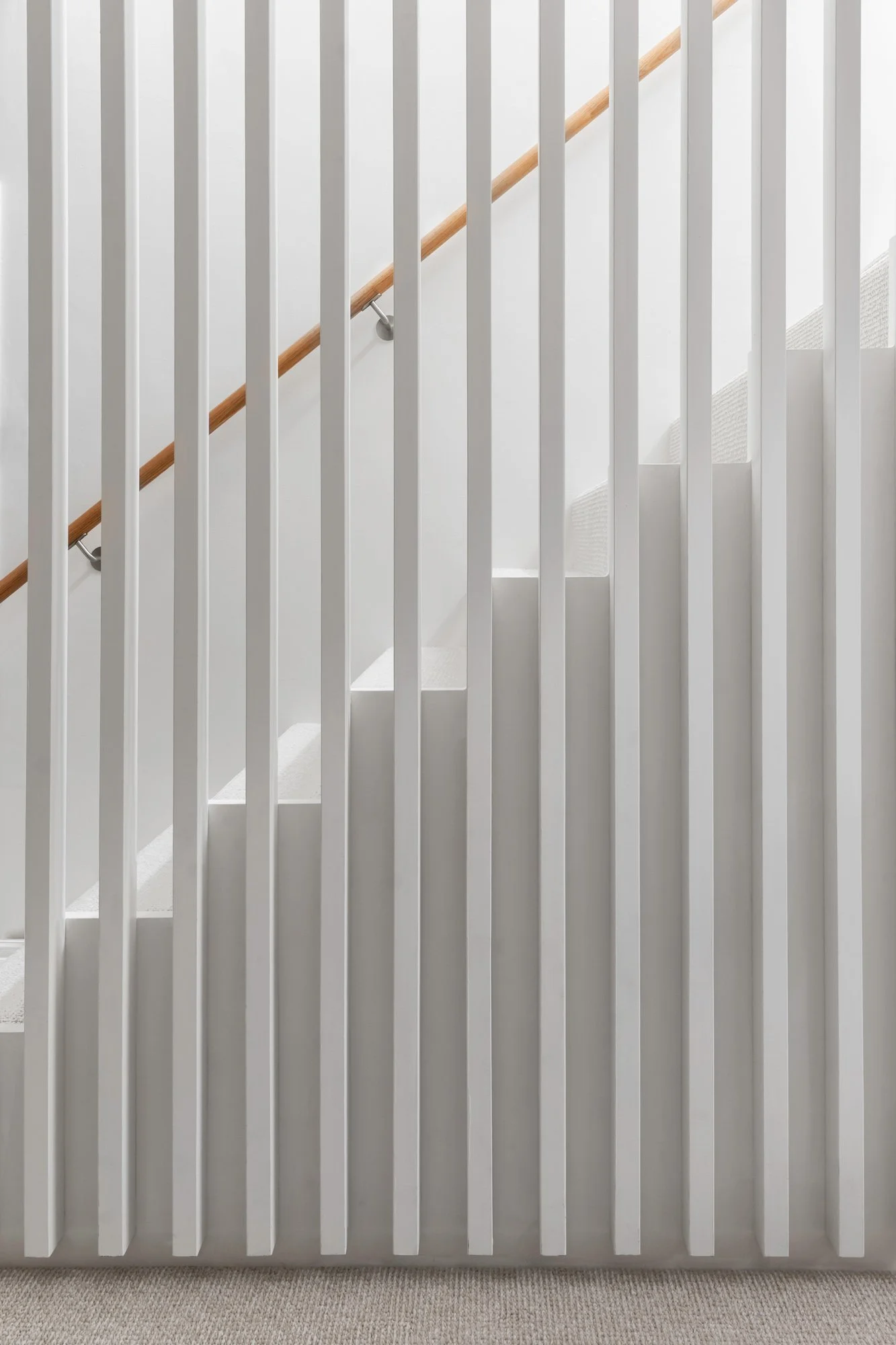 A front view of white, floor-to-ceiling vertical slats with wide 10-centimeter gaps, seamlessly blending the staircase with the room while maintaining a subtle spatial boundary.