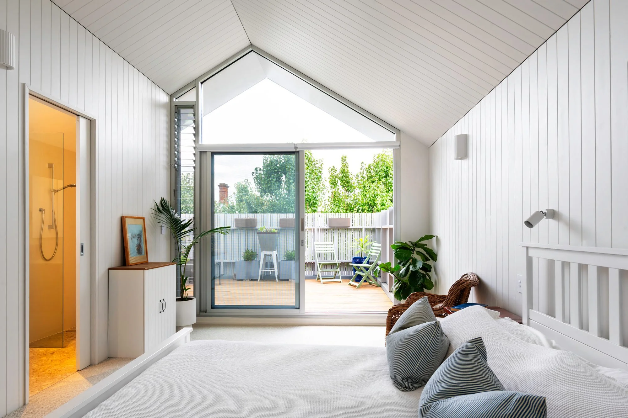 Wide-angle view of a top-floor bedroom featuring an asymmetric vaulted ceiling and white wood cladding on the walls and ceiling, facing a floor-to-ceiling angled window.
